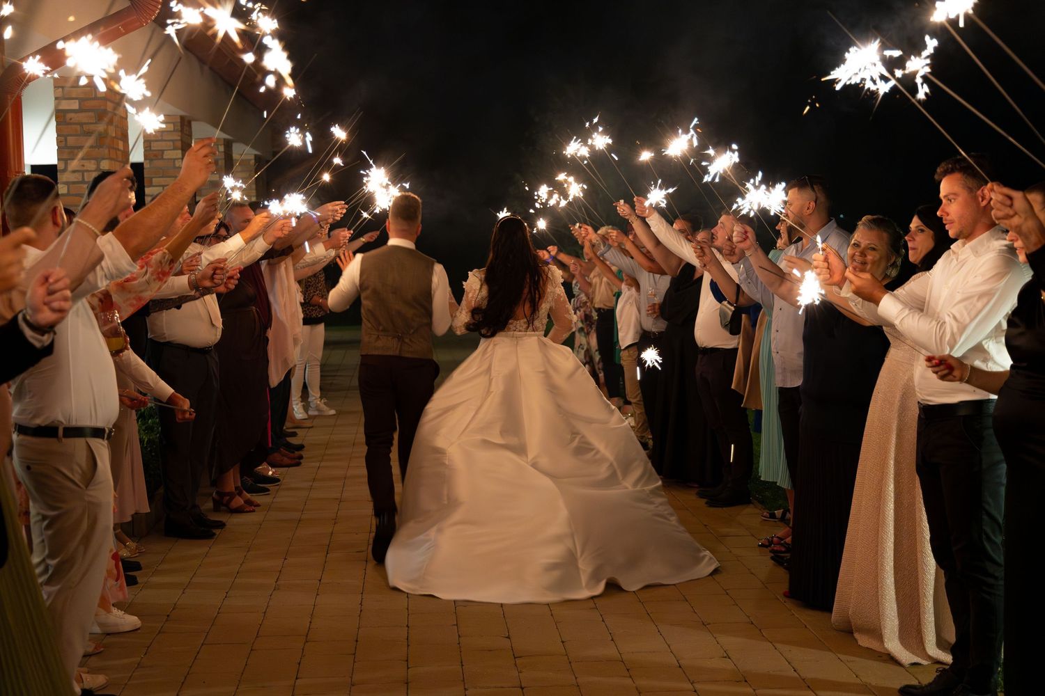 Wedding guests form sparkler exit tunnel for celebrating newlyweds.
