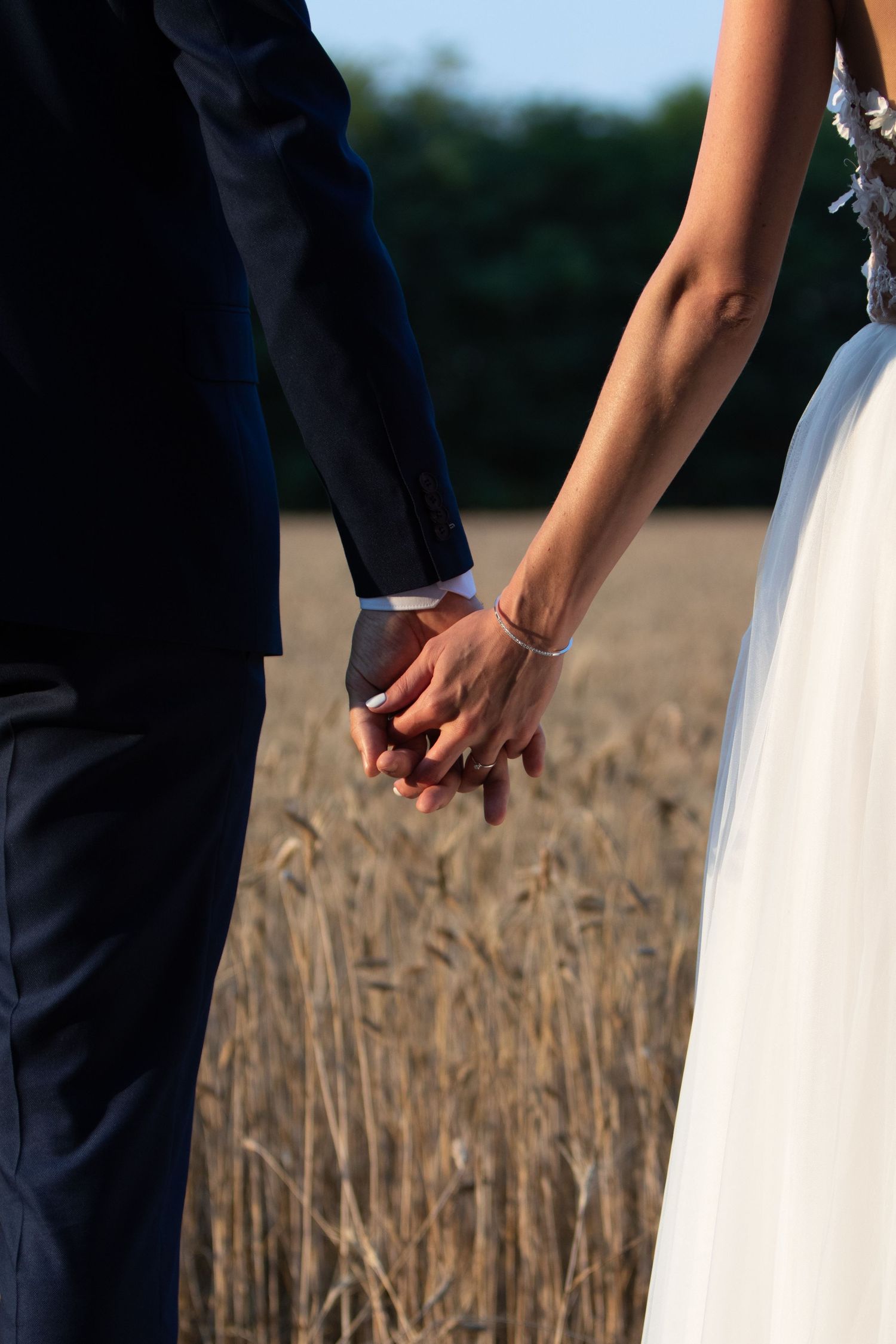 Close-up of a couple holding hands in a wheat field on their wedding day.