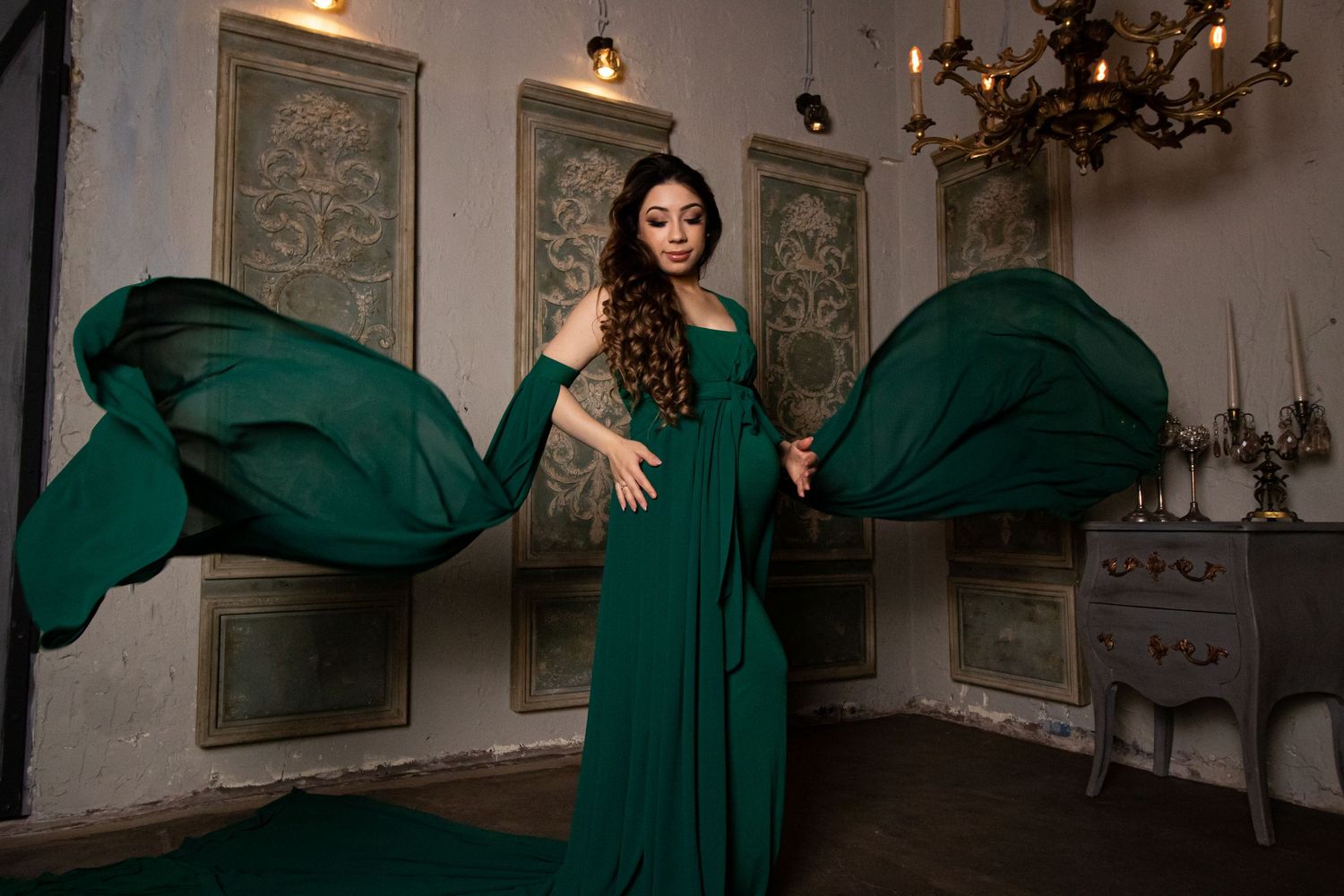 Elegant maternity photos featuring flowing emerald green dress in vintage room with ornate wall panels.