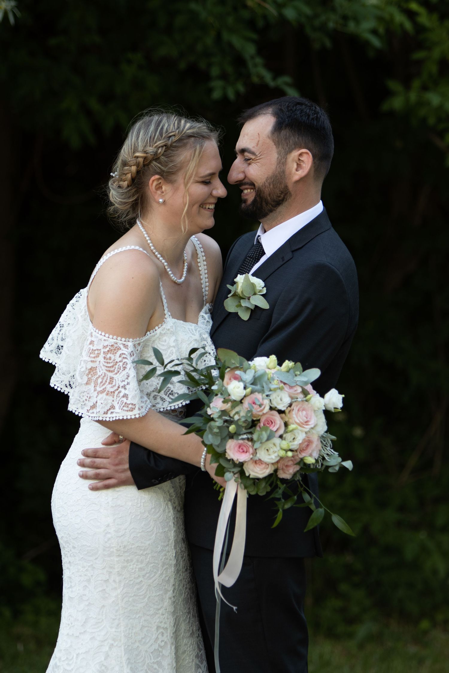 A romantic wedding portrait of a couple sharing a joyful moment with a beautiful floral bouquet in an outdoor setting.