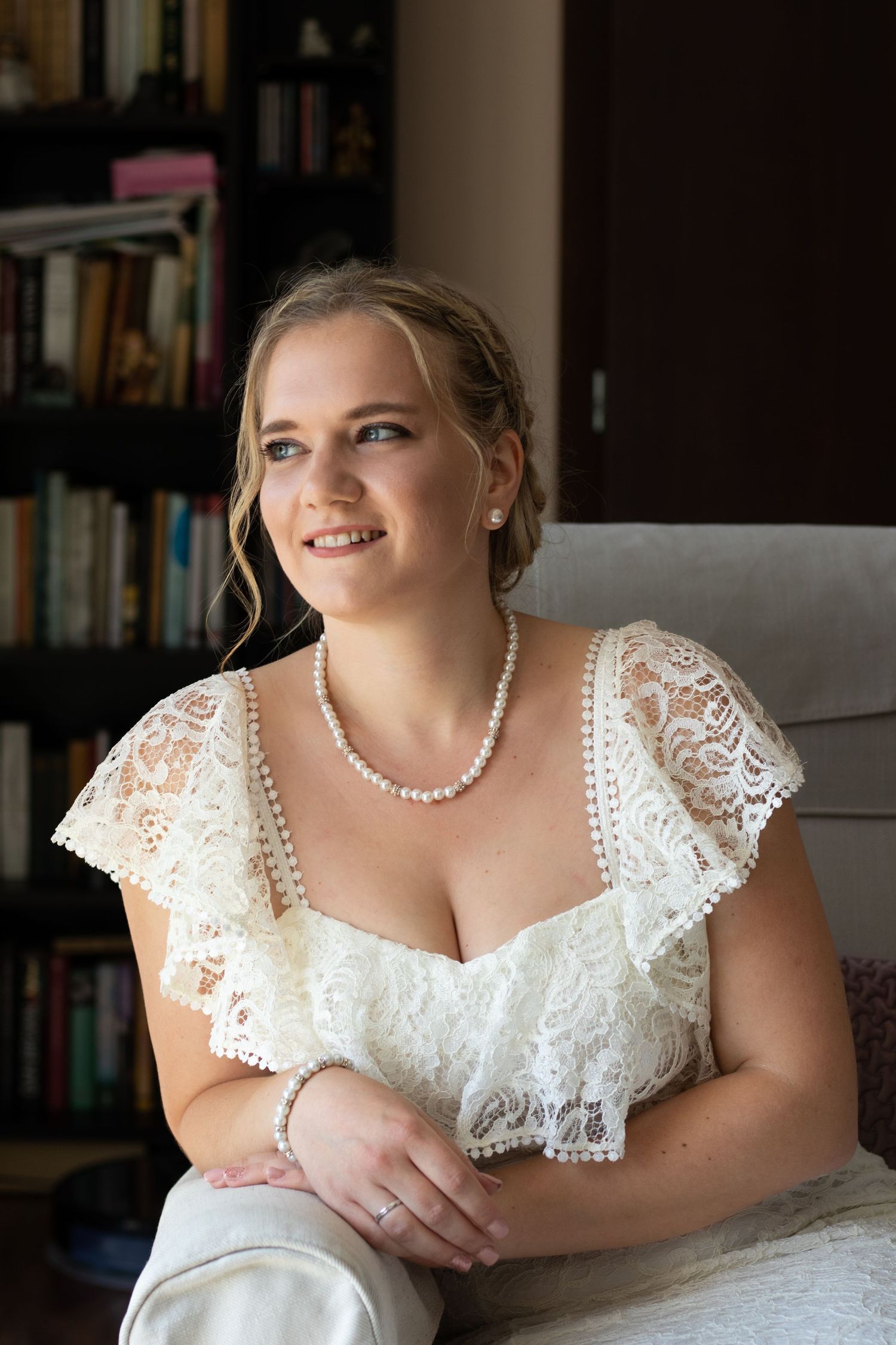 A bride in a lace cap sleeve wedding dress poses by a window.