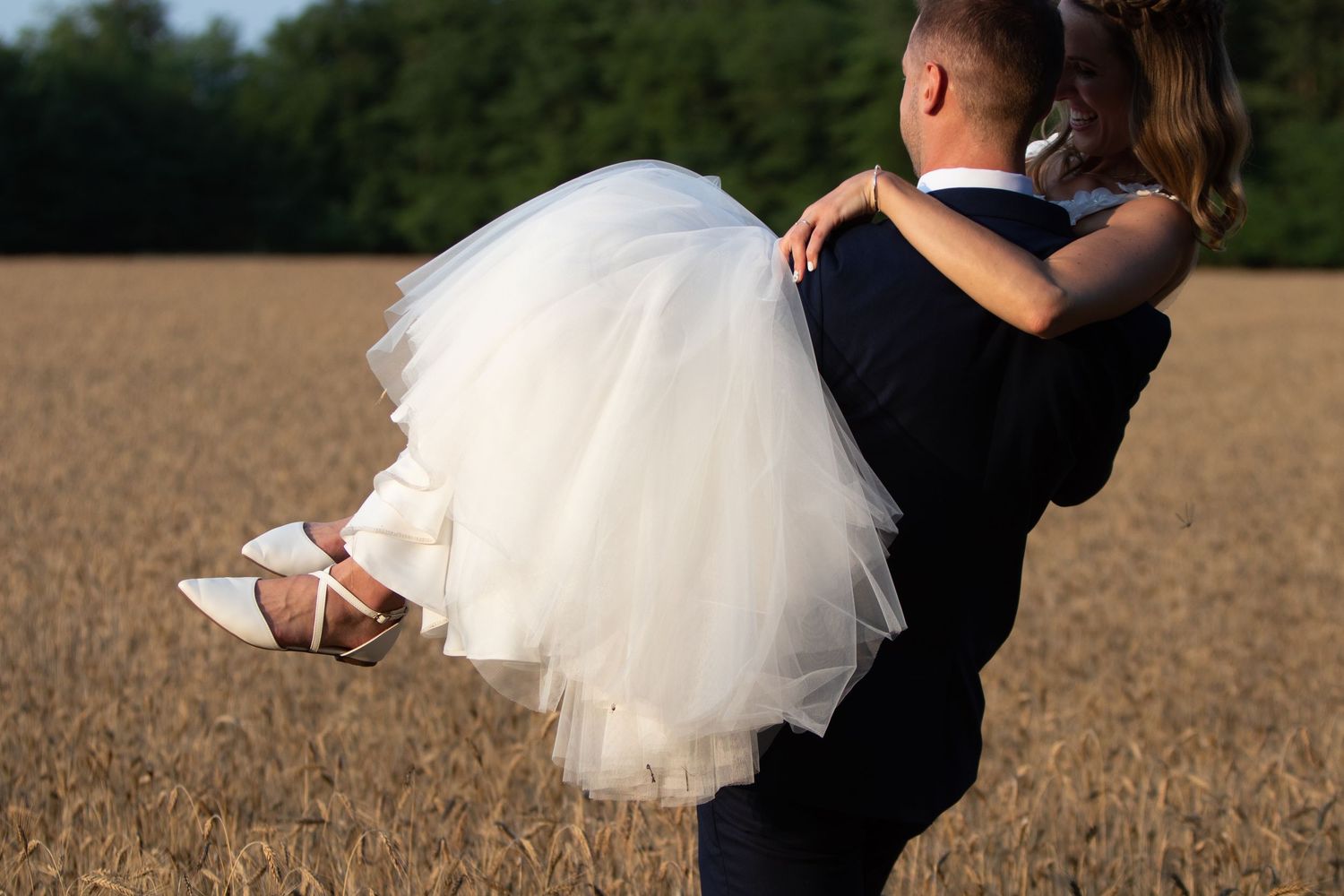 Romantic couple dancing in formal wear against rural field backdrop.