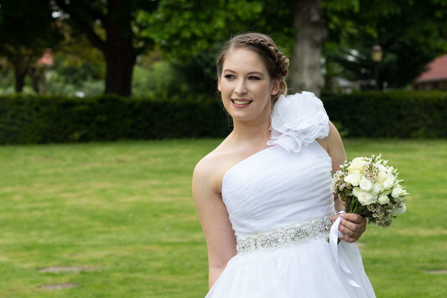 Bride holding a white floral bouquet while walking through a lush garden setting.