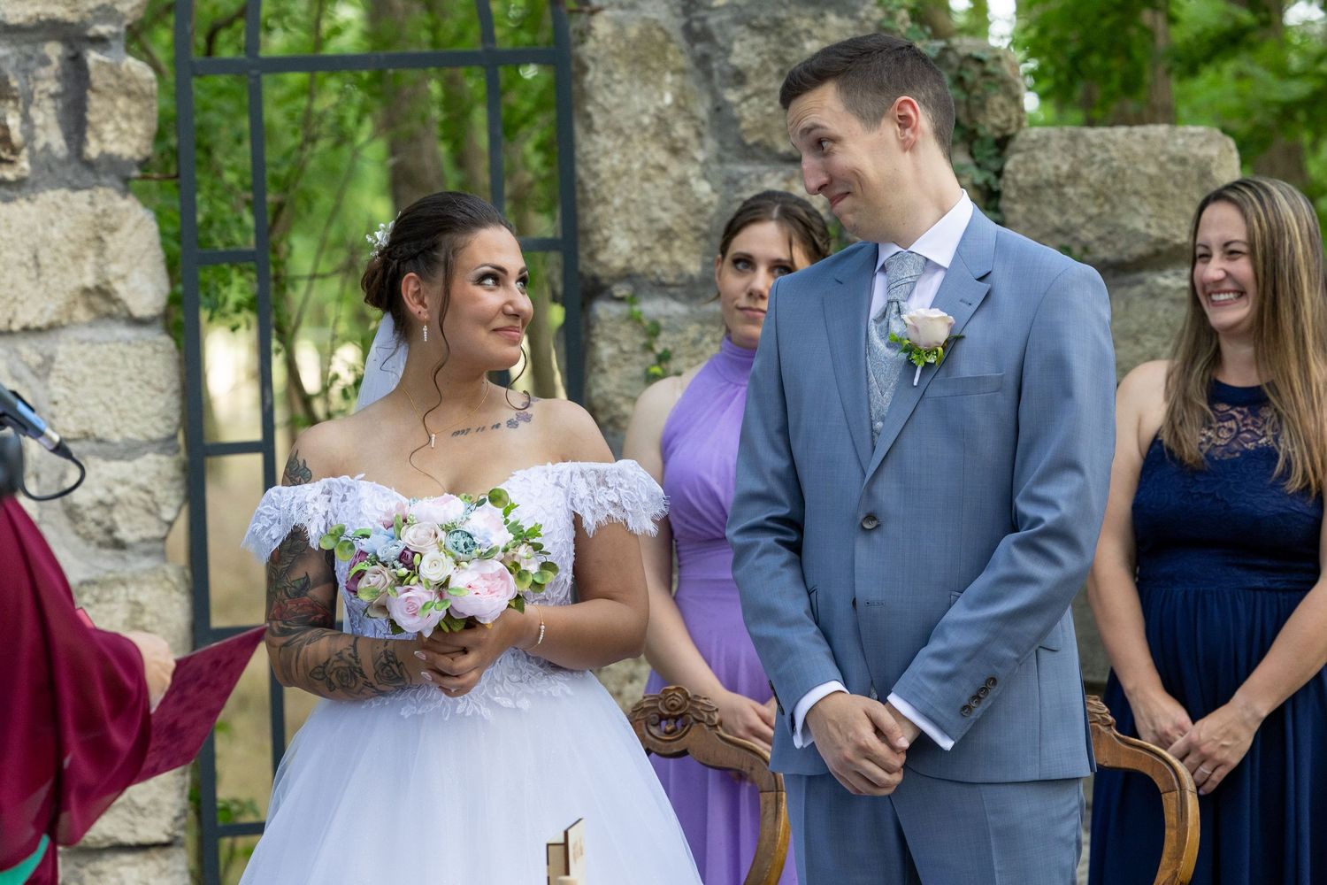 Couple exchanges vows during outdoor wedding ceremony with stone wall backdrop.