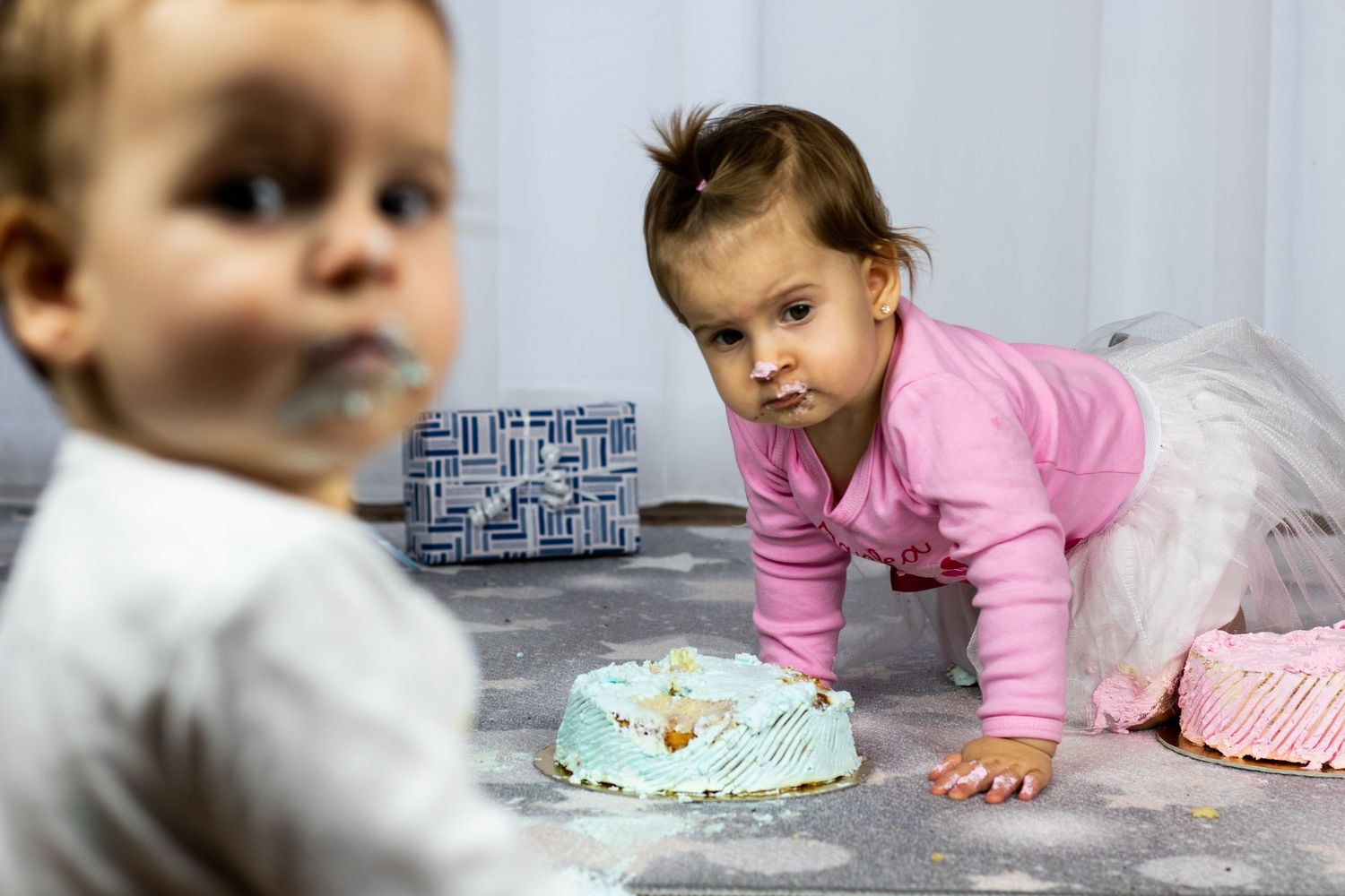 Baby exploring cake on floor with pink and blue party decorations visible.