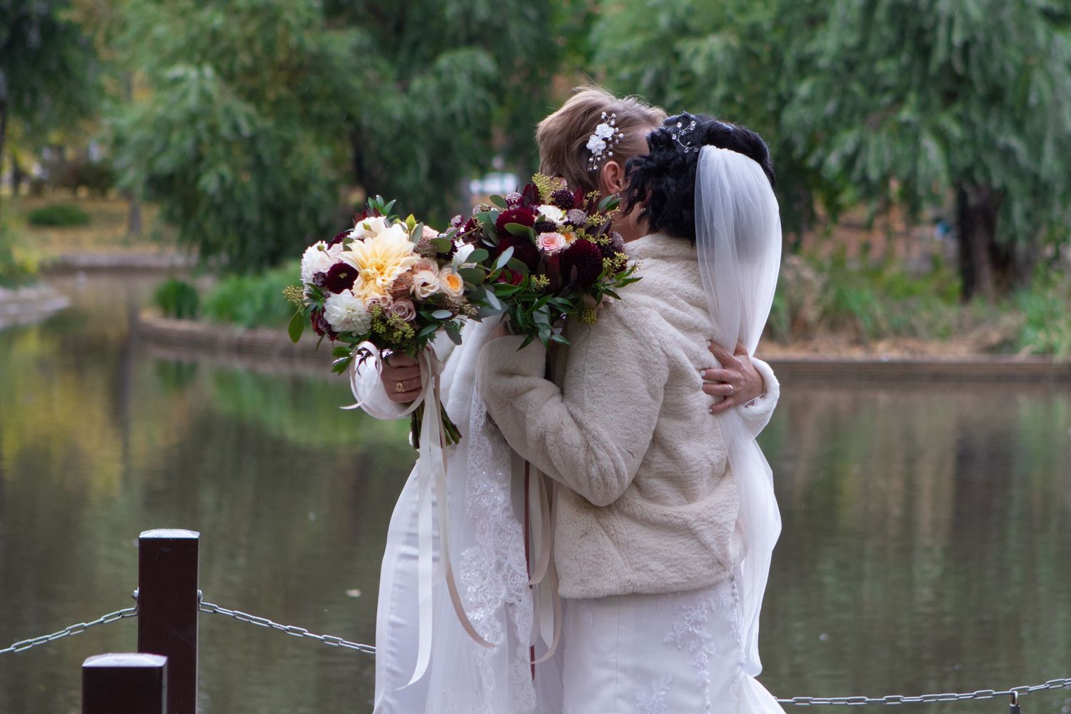 Wedding bouquet held against white dress near a serene lake.