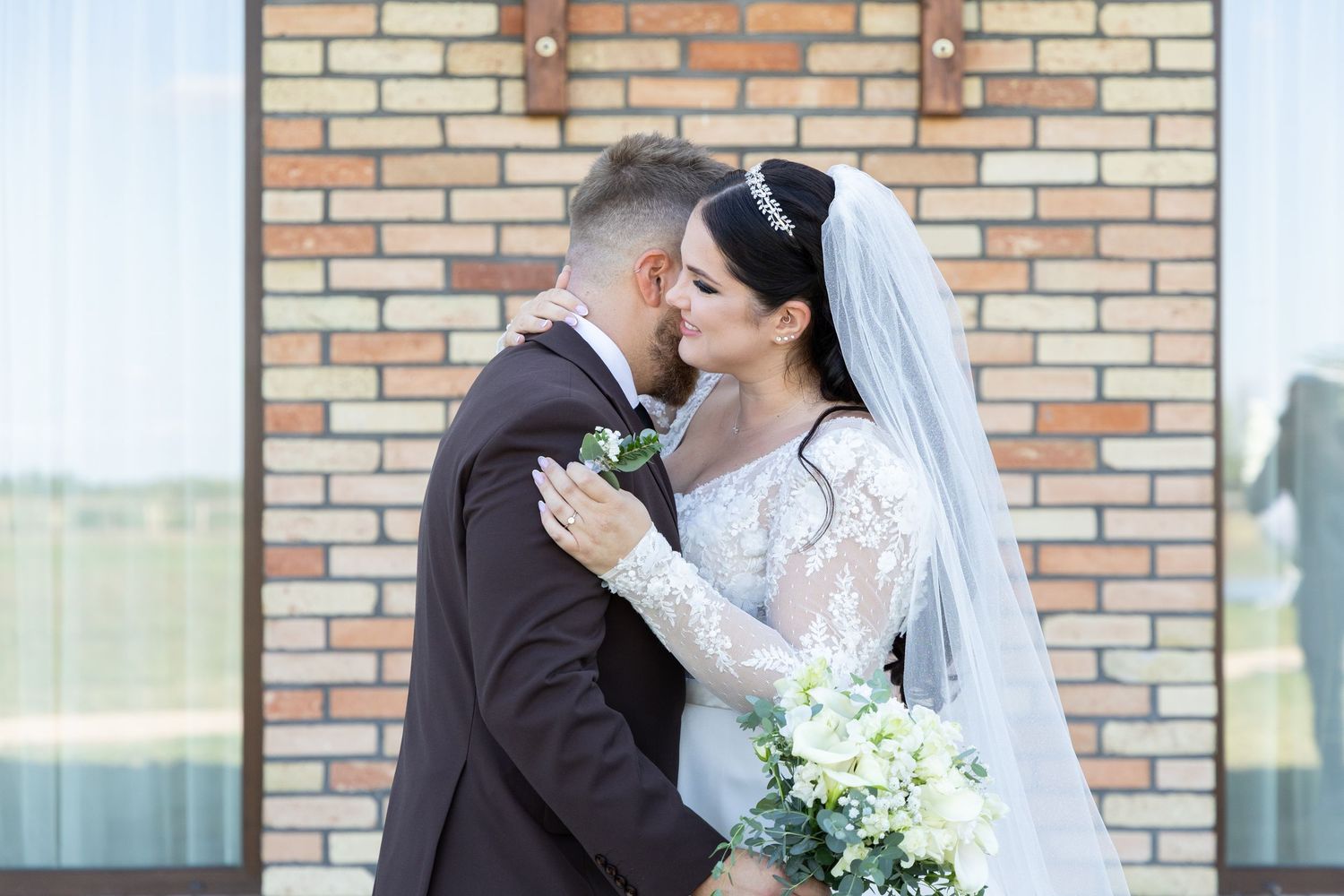 Romantic wedding portrait against brick wall with white bouquet and lace dress details.