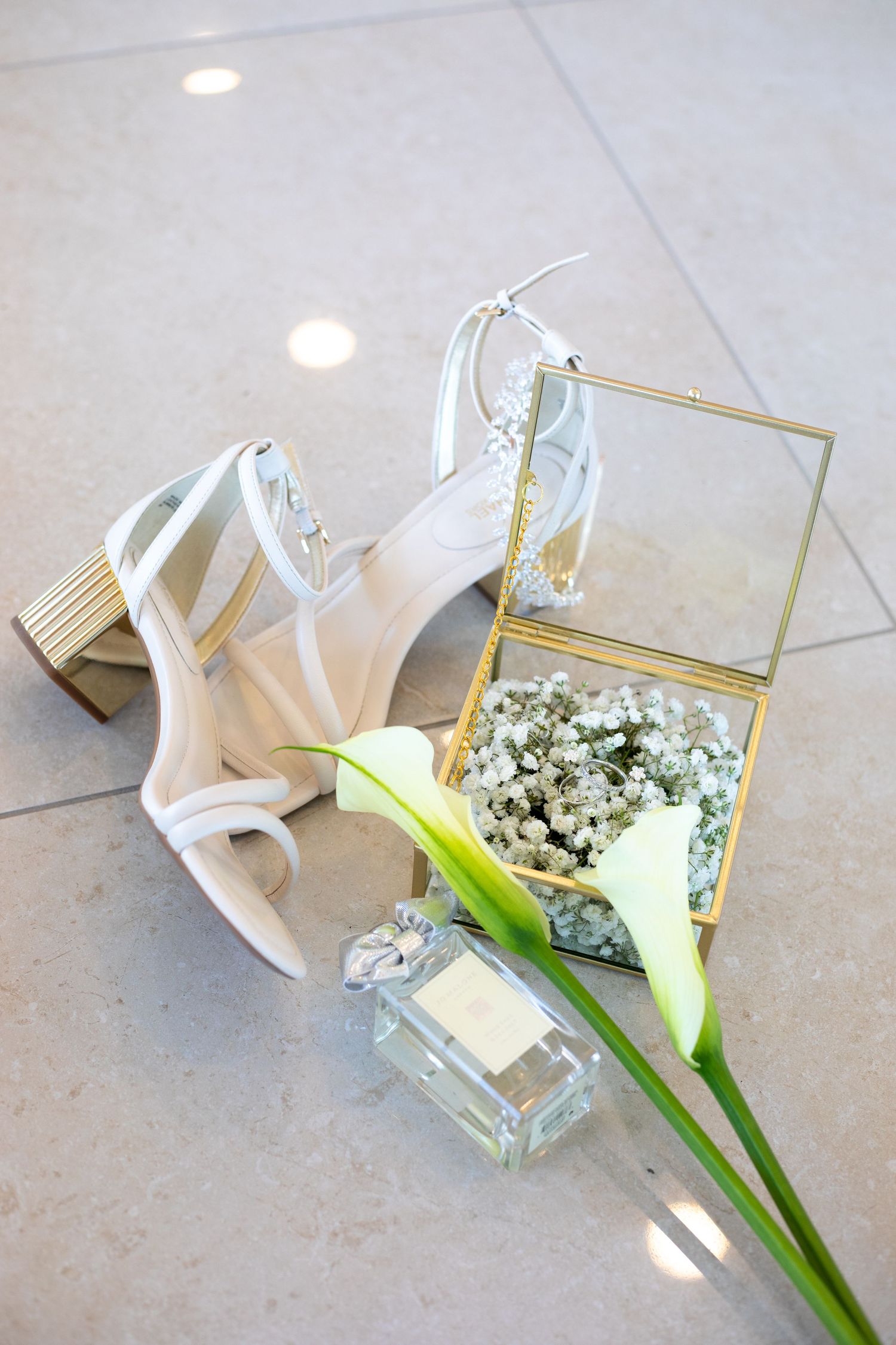White calla lily and baby's breath arranged in a modern glass vase on a light surface.