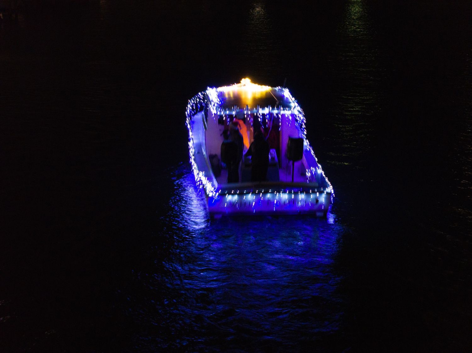 Drone photo of a single decorated boat glowing with colorful lights at night.