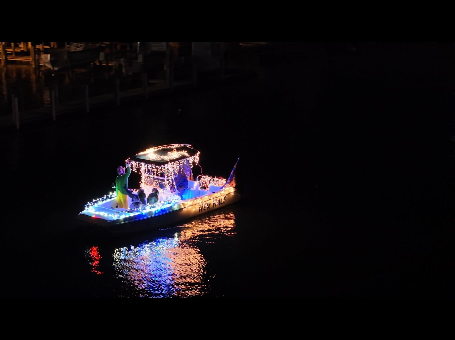Drone photo of a decorated boat at night surrounded by darkness and reflections.