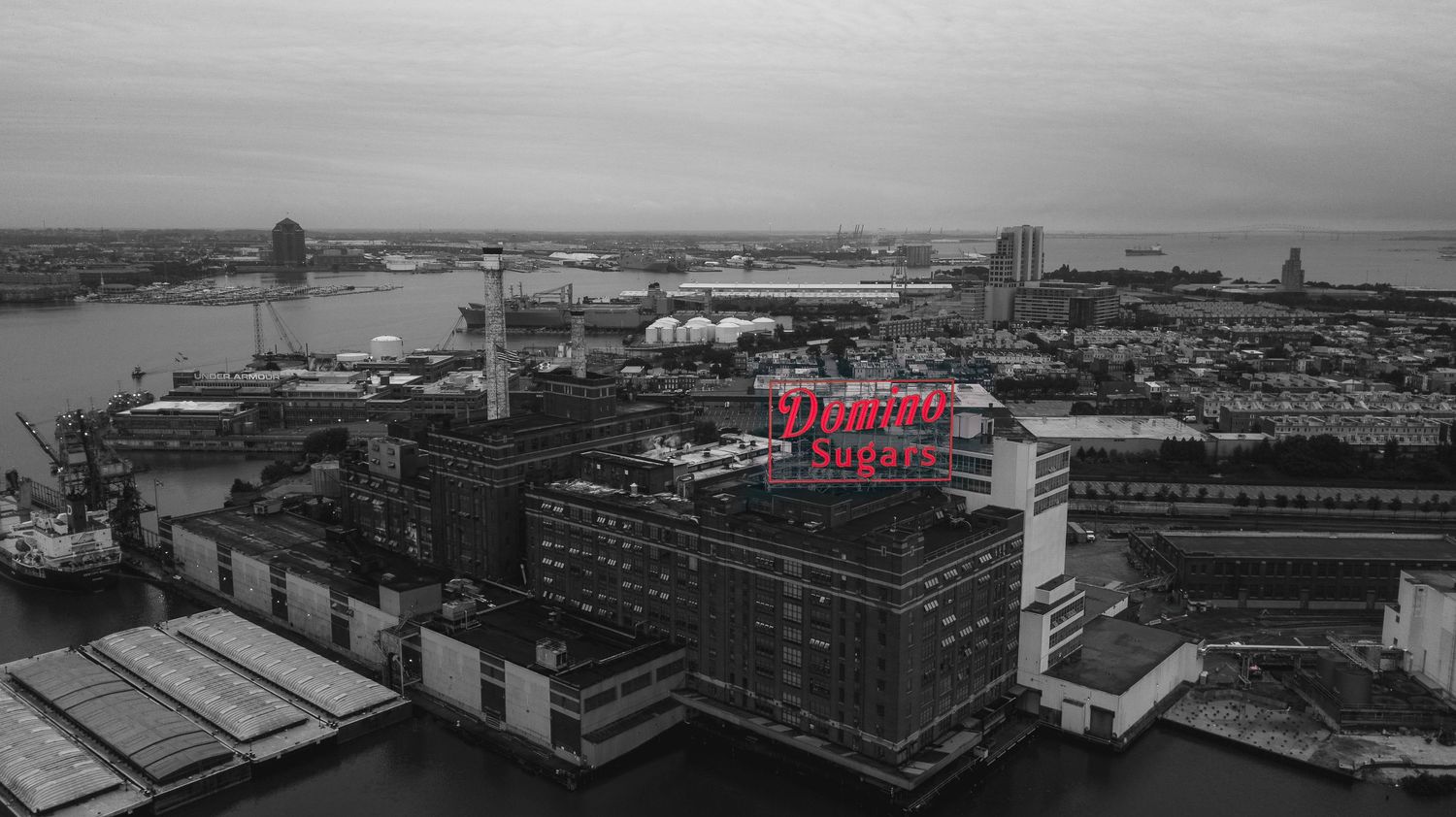 Black-and-white aerial view of Baltimore with Domino Sugar sign light up in red.