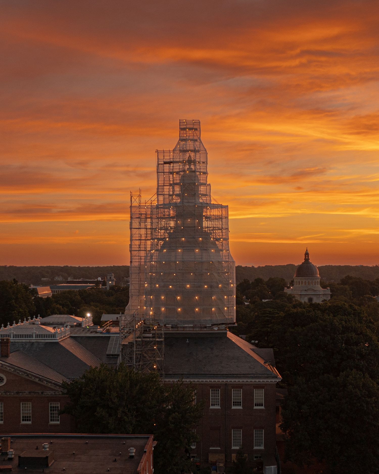 Drone photo of the Maryland State House with scaffolding at sunset with warm sky and city surroundings.