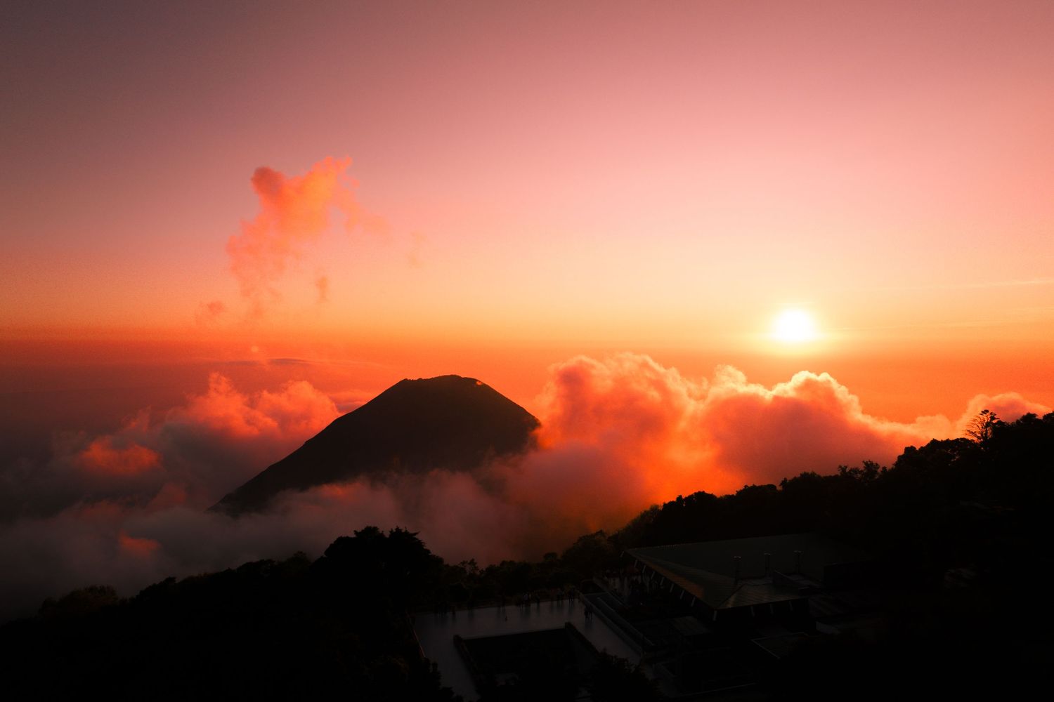 A aerial photograph during a fiery sunset of a volcano surrounded by clouds in El Salvador.