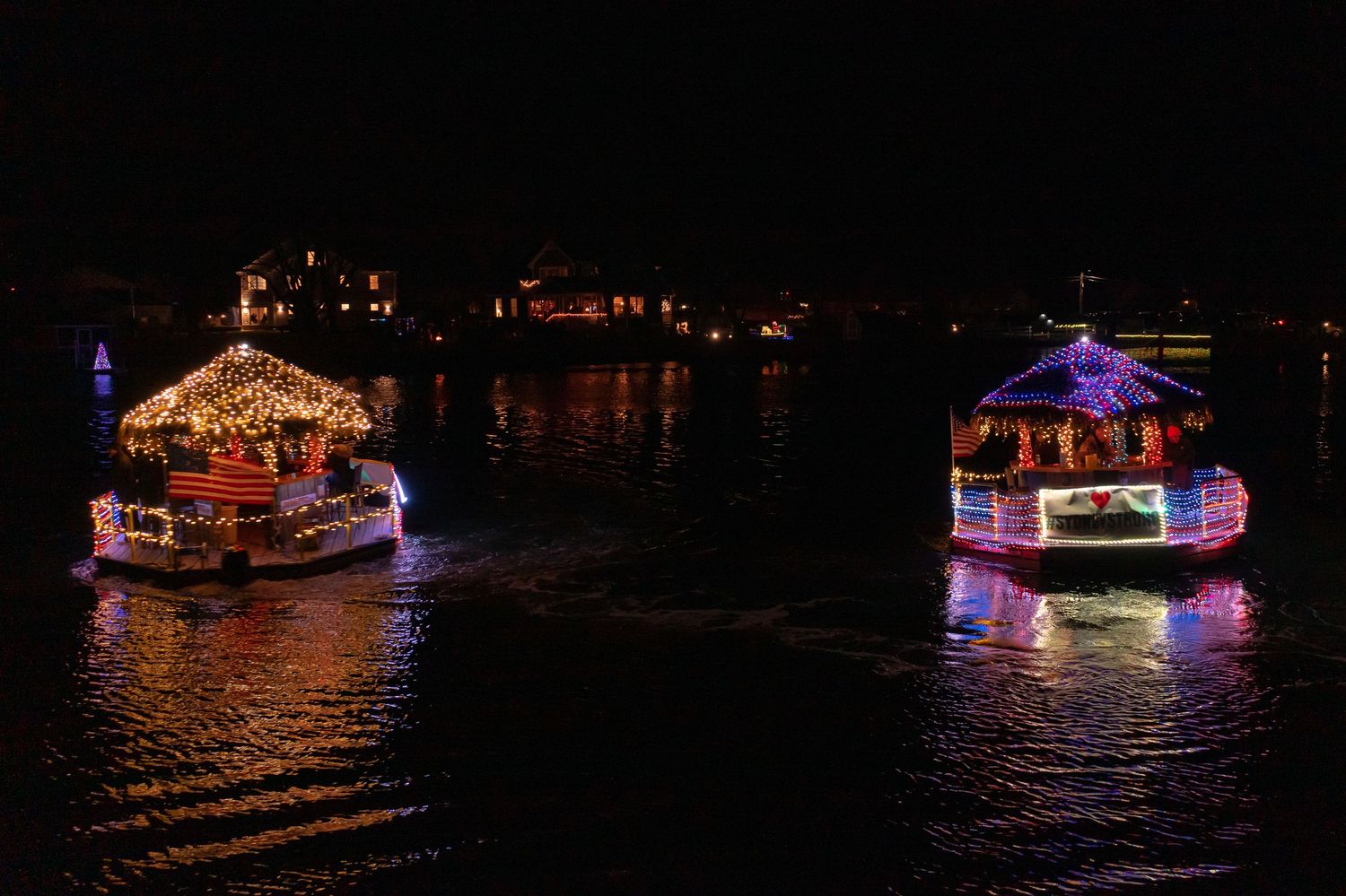 Drone photo of two decorated boats at night surrounded by darkness and reflections.