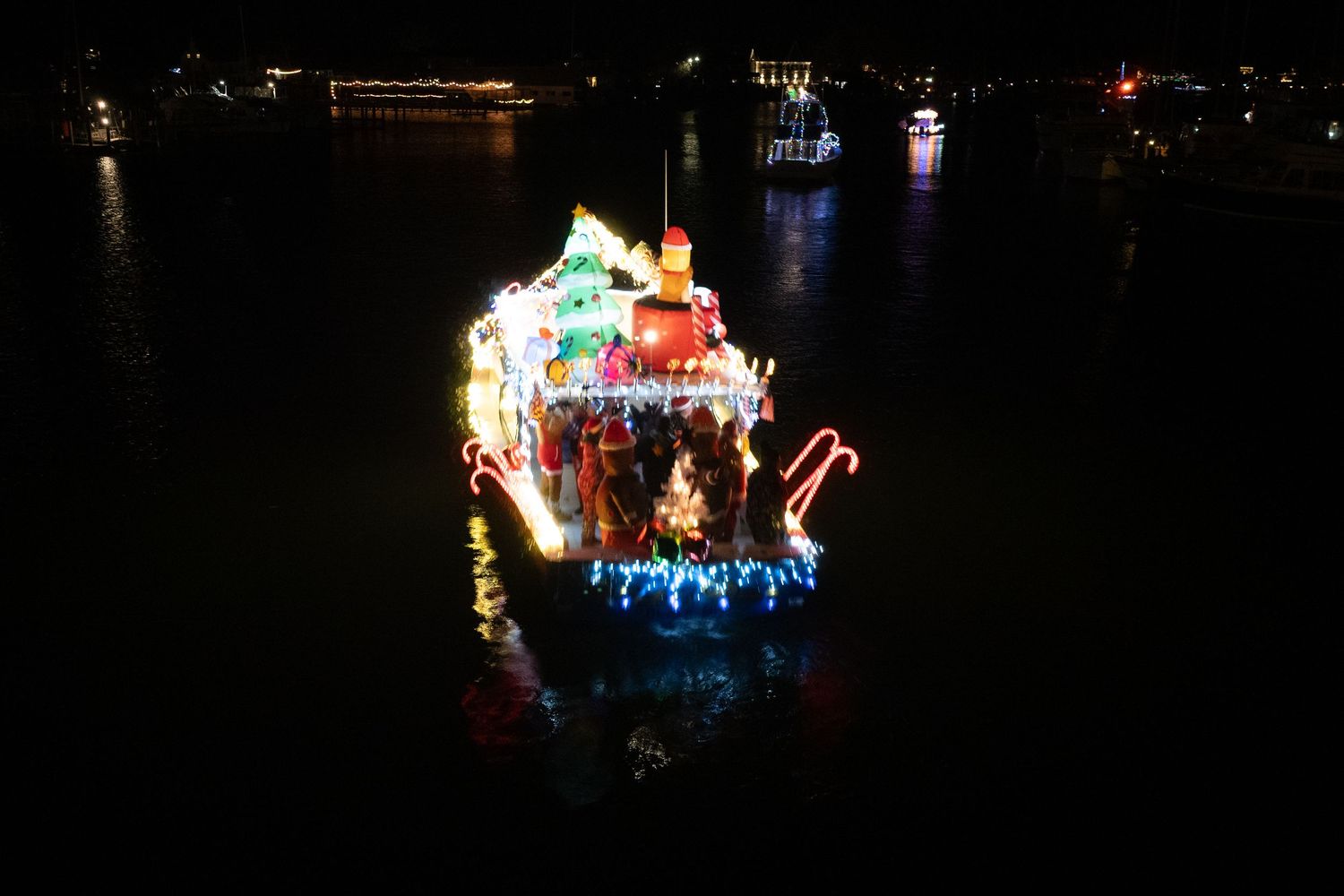 Top-down aerial view of a festively lit boat moving through dark water.