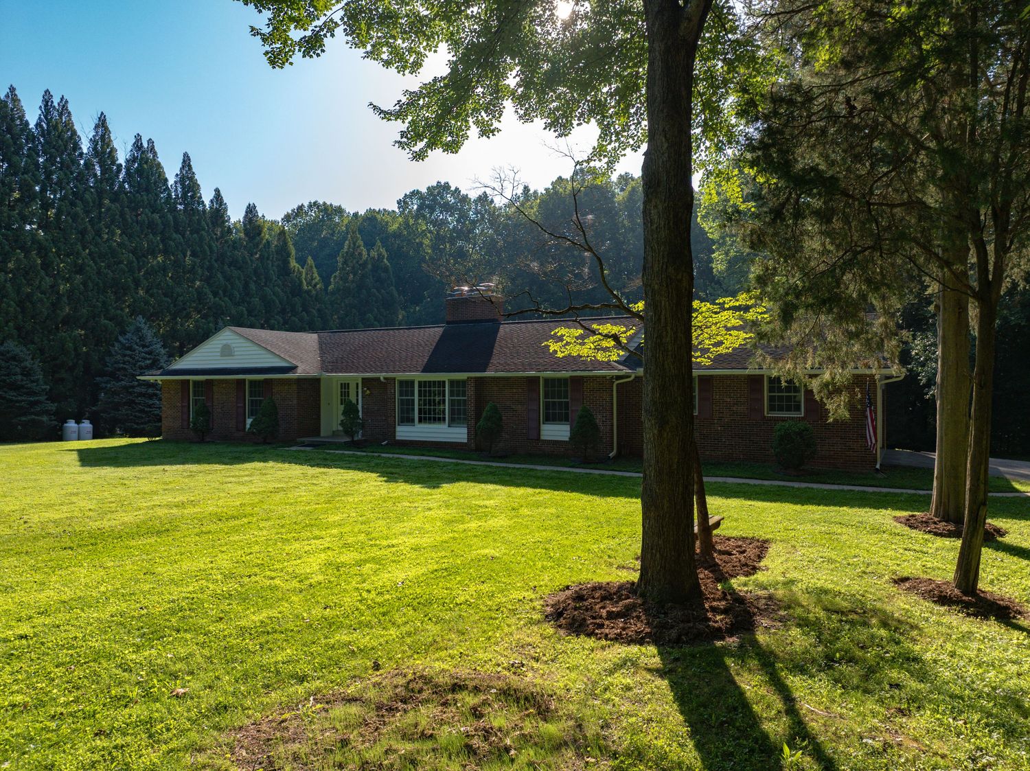 Wide aerial photo of a modern house set within a landscaped green lawn and trees.