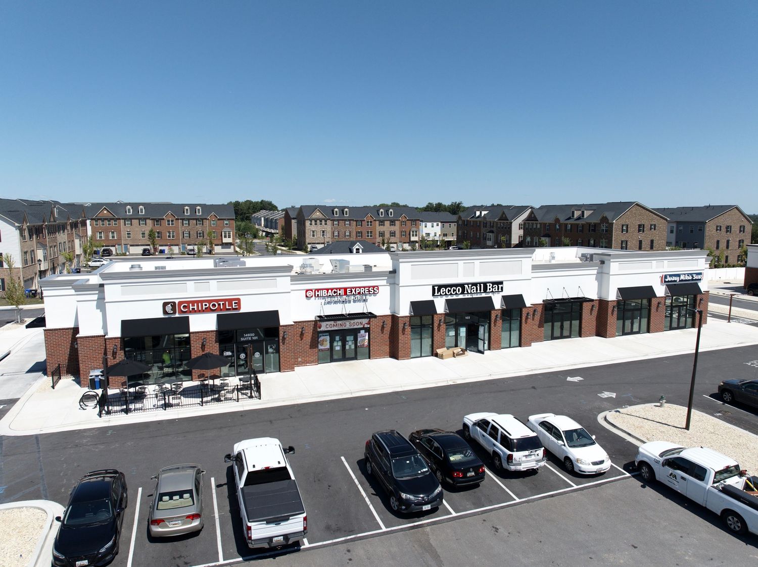 Drone photo of a commercial plaza with multiple storefronts and parked cars.