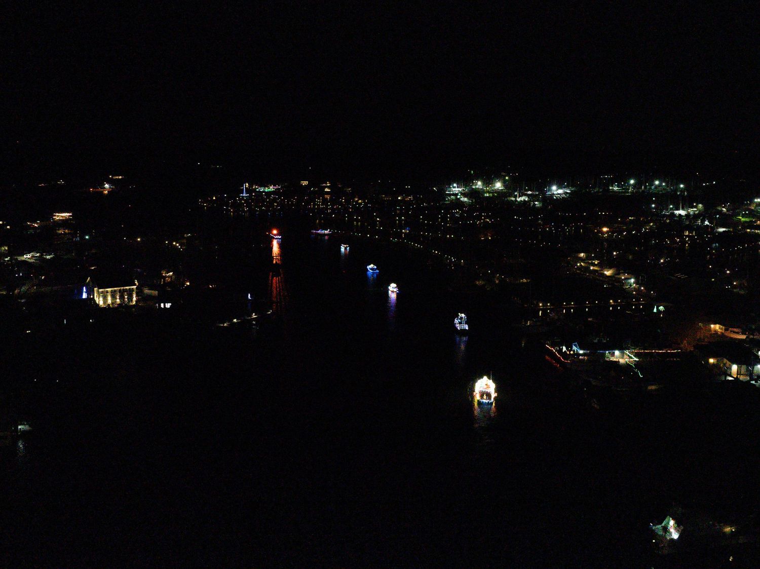 Nighttime aerial view of illuminated boats gathered on the water during a lighted parade.