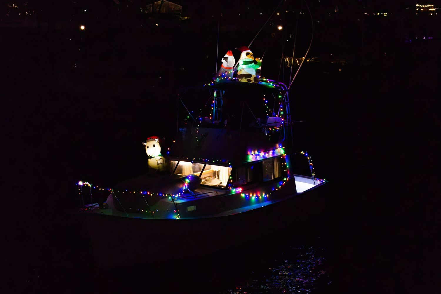 Night aerial shot of a brightly lit boat with colorful decorations reflecting on the water.