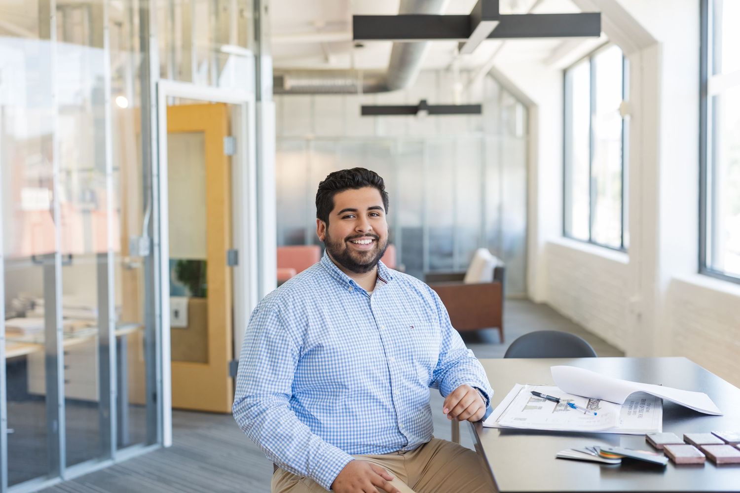 Professional headshot of the founder of POV TXNY, seated in an office setting in front of a table with papers.