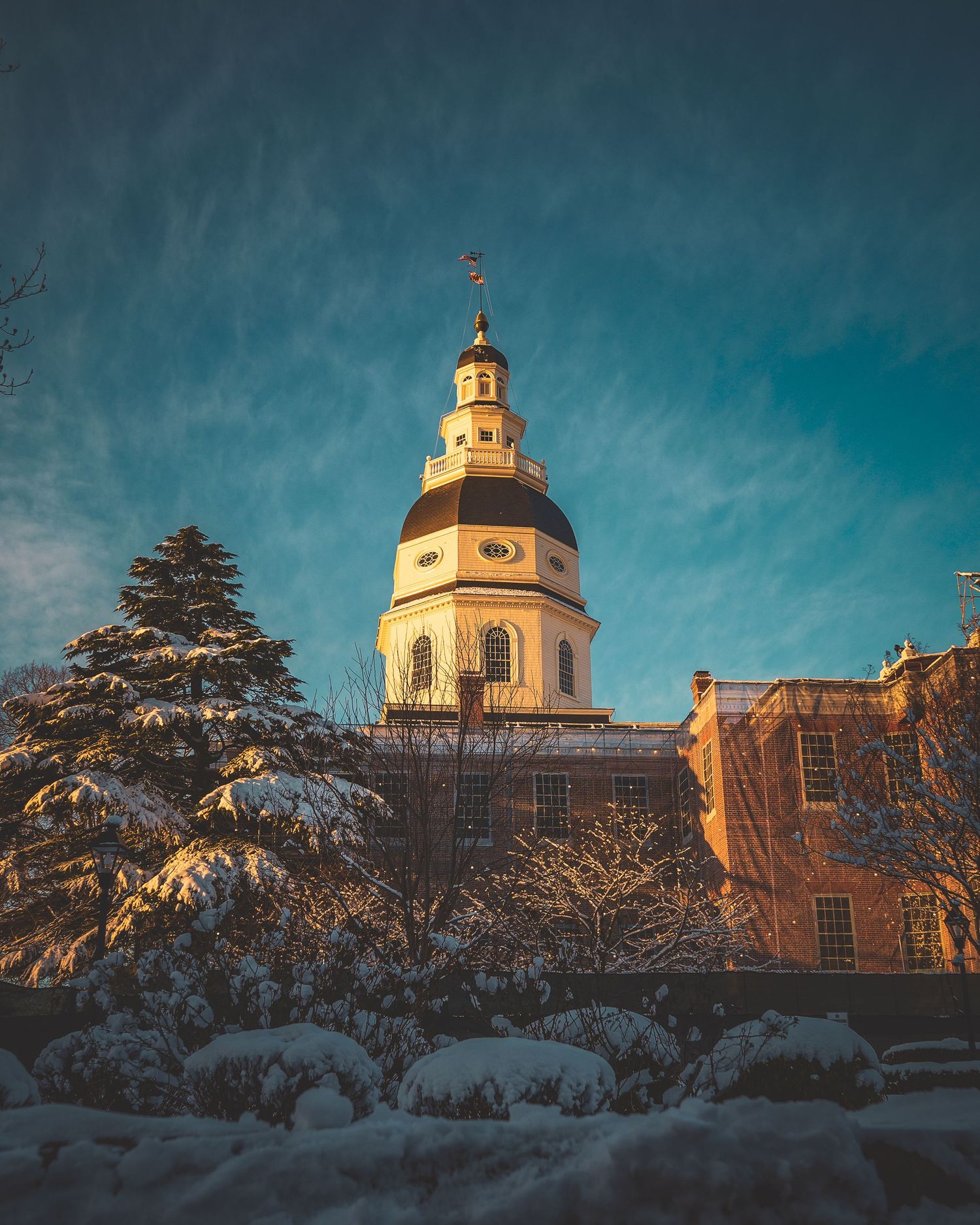 Snow-covered capitol building photographed during the morning with glowing lights and winter atmosphere.