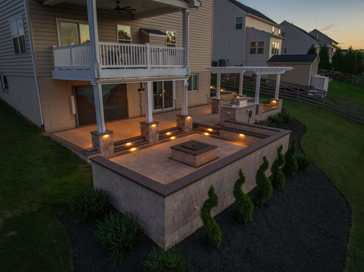An aerial photograph of a finished beautiful and custom backyard patio during sunset with lights throughout.