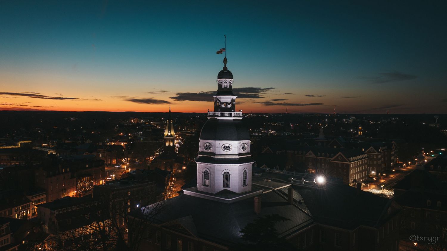 Nighttime aerial view of a domed capitol building illuminated against the surrounding city lights in Annapolis.