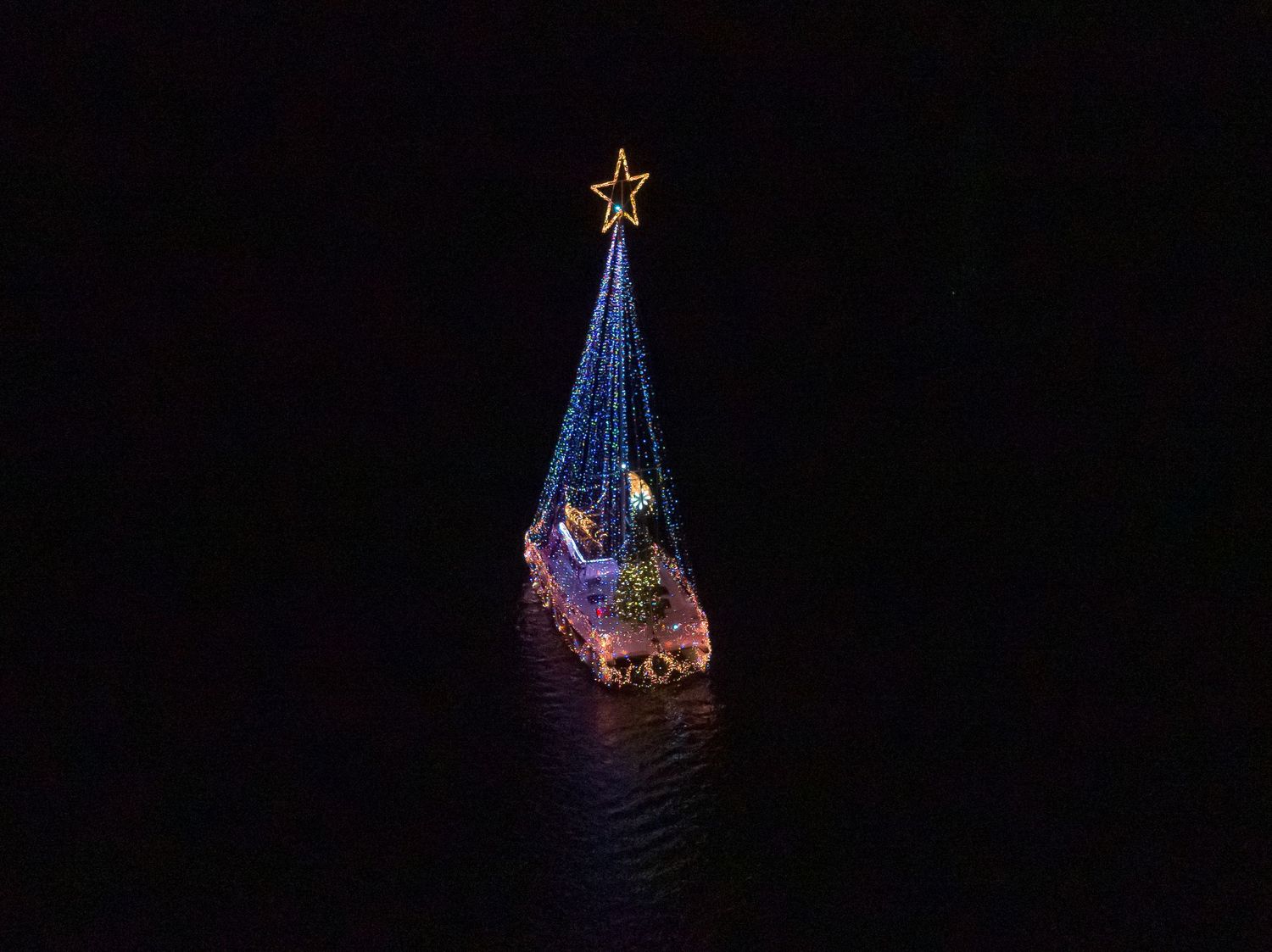 Drone photo of a decorated boat at night surrounded by darkness and reflections.