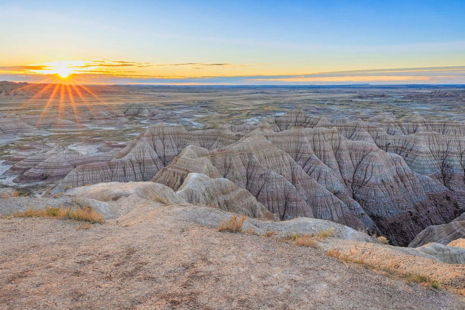 Dramatic sunrise over the rugged Badlands National Park landscape with eroded rock formations stretching to the horizon.