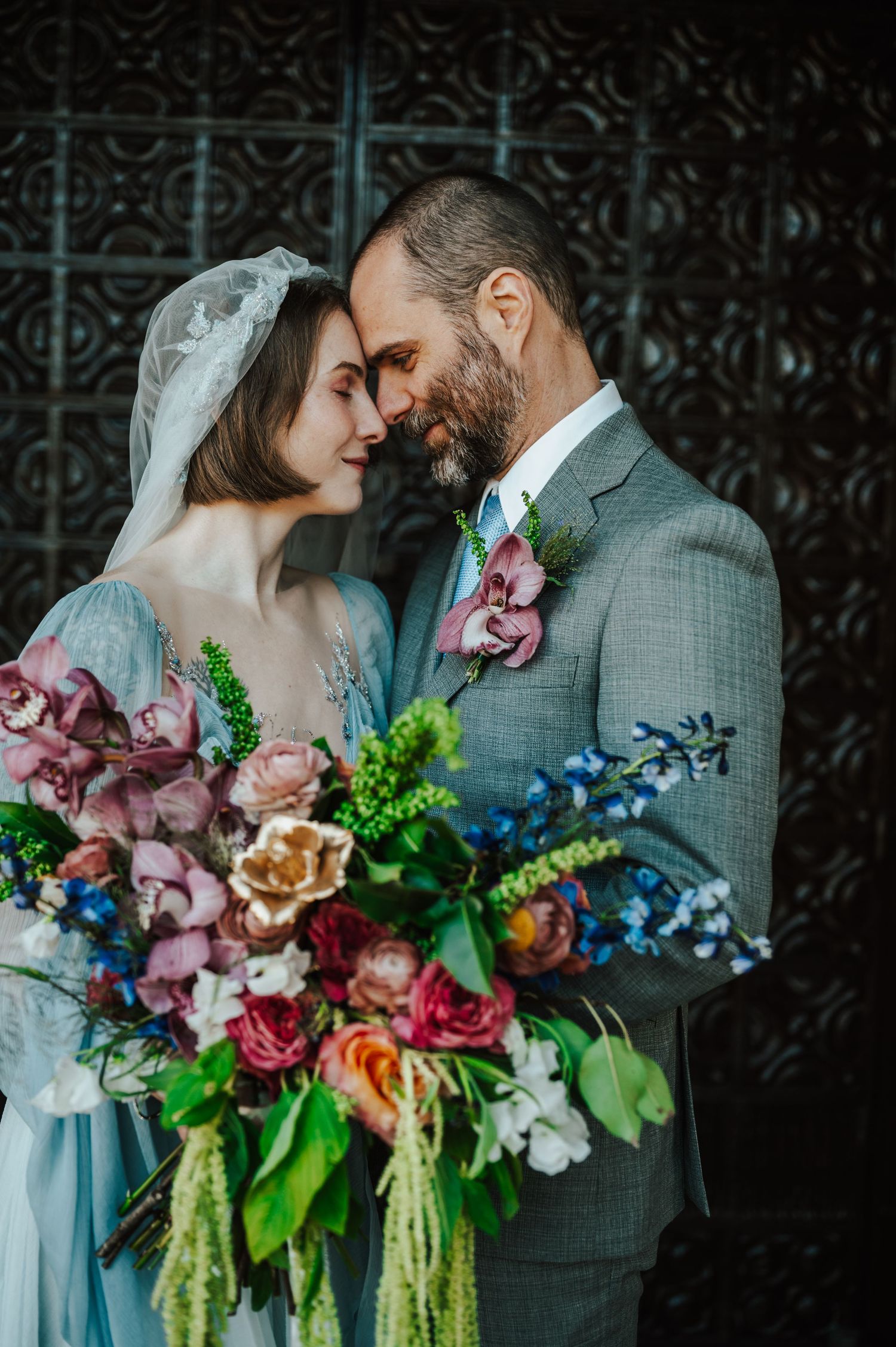 A romantic wedding couple shares an intimate moment with a vibrant bouquet of pink, blue and green flowers.