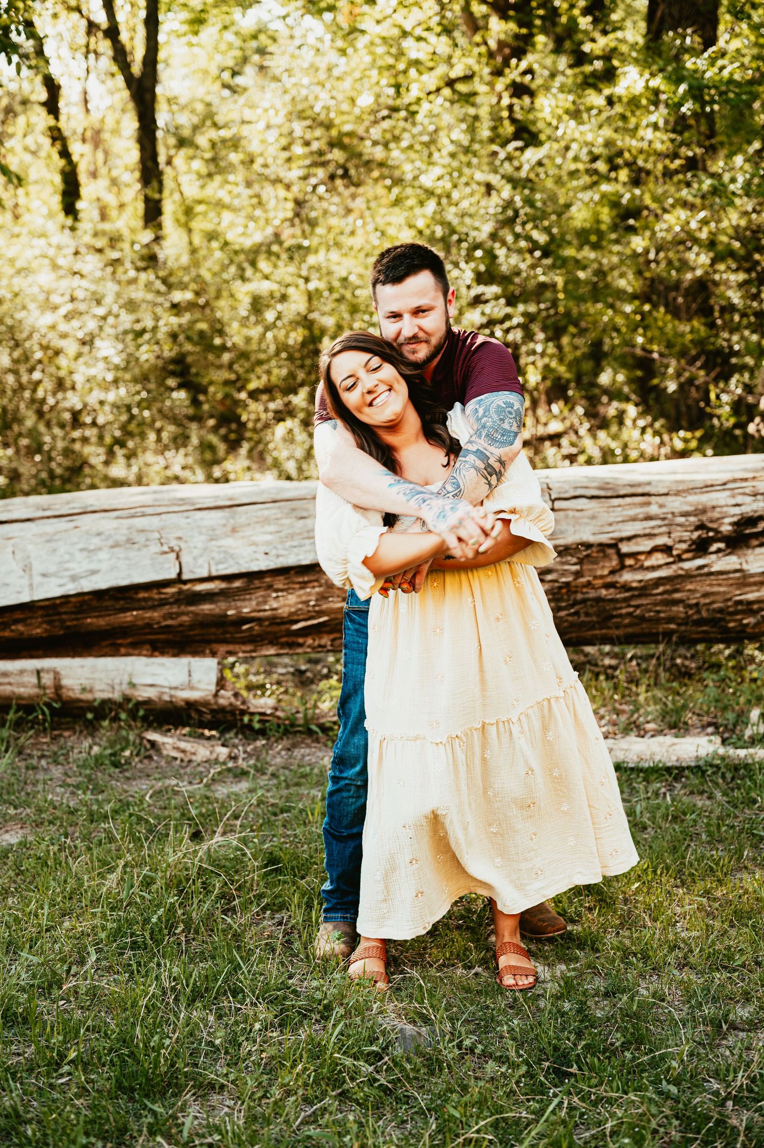 Couple embracing and laughing together in a sunny outdoor setting with wooden fence.