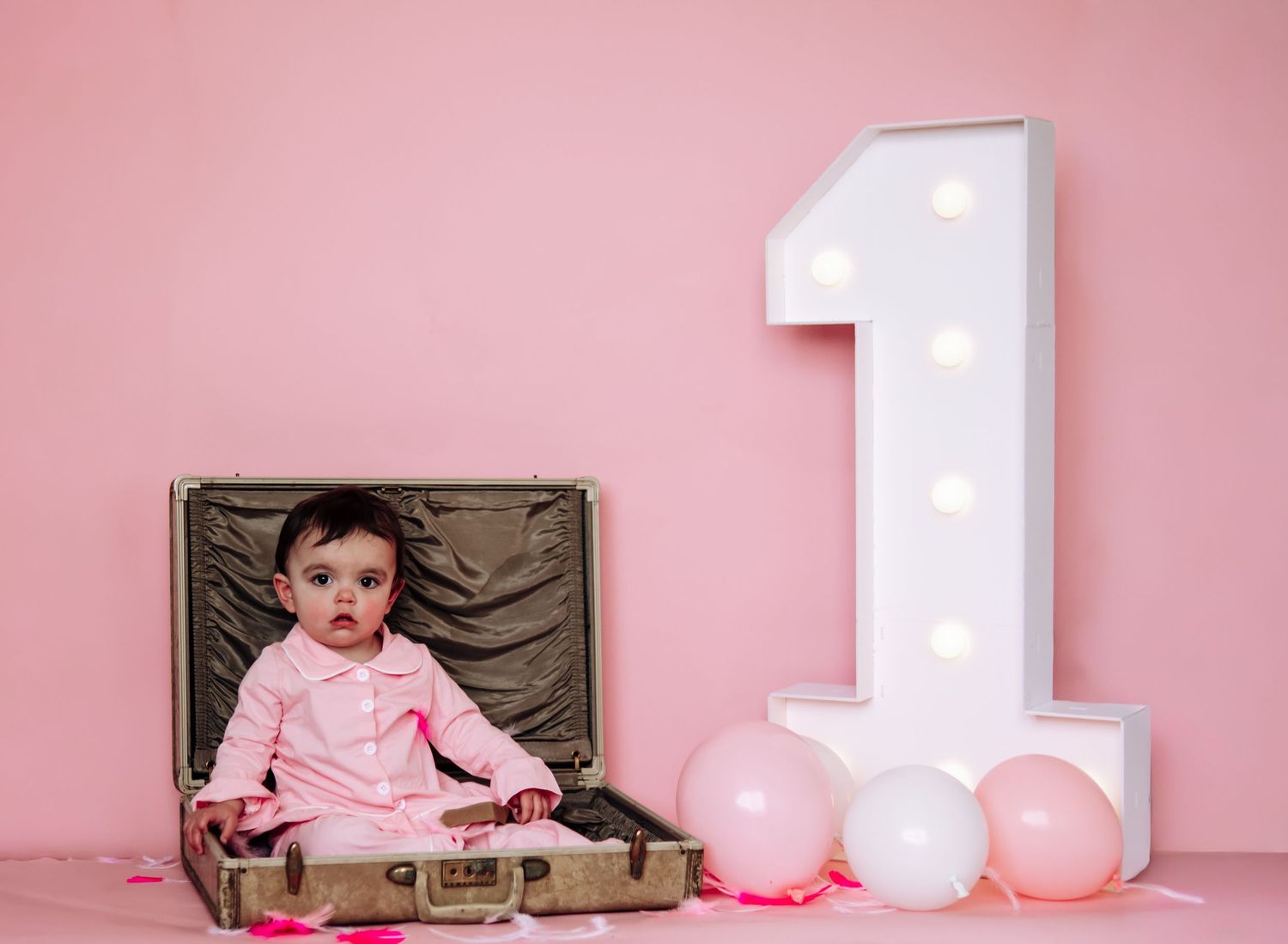 Monthly milestone photos show baby growth from one to twelve months with pink balloons and white number decorations.