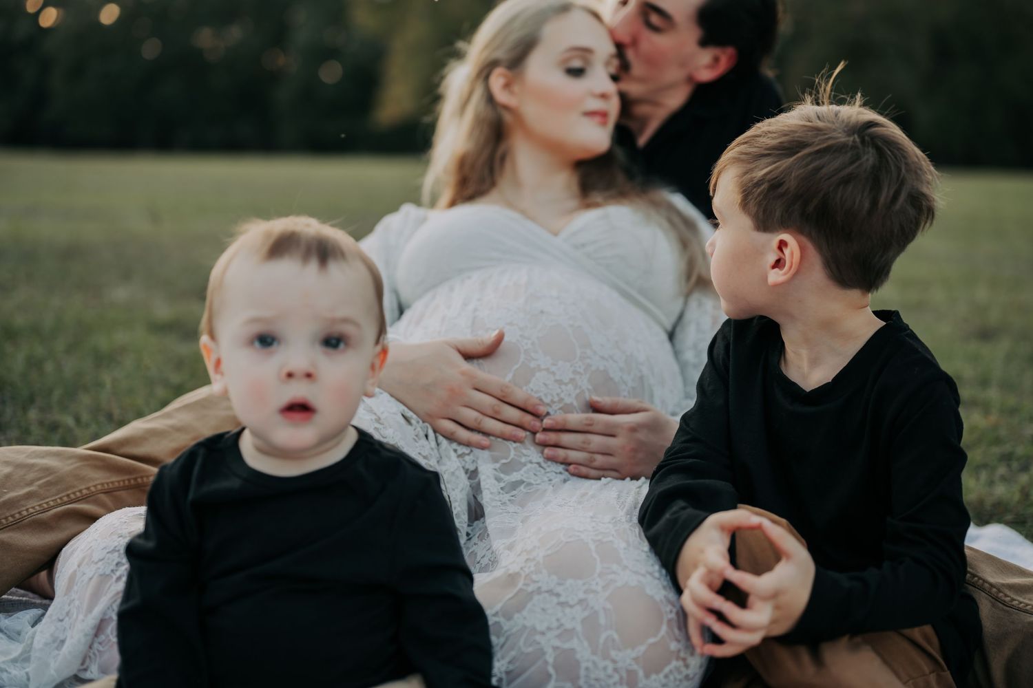 Family sharing tender moment in outdoor field during sunset photoshoot.