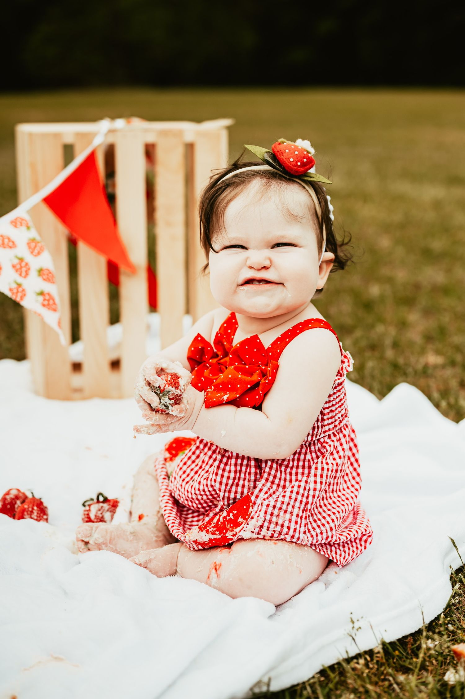 Baby in red gingham outfit lying on white blanket with festive decorations.