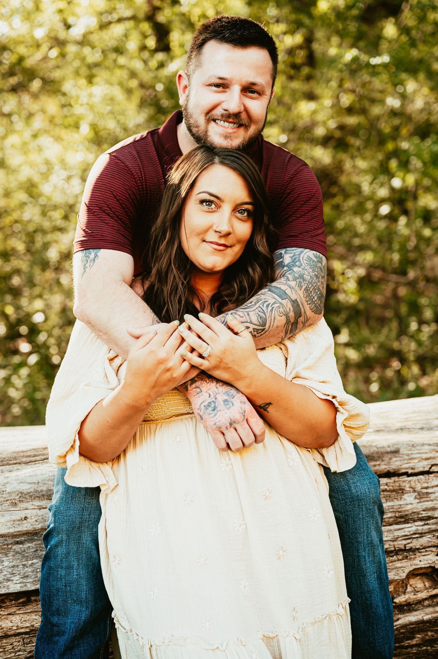 Romantic couple embracing while sitting on a rustic log outdoors in golden sunlight.