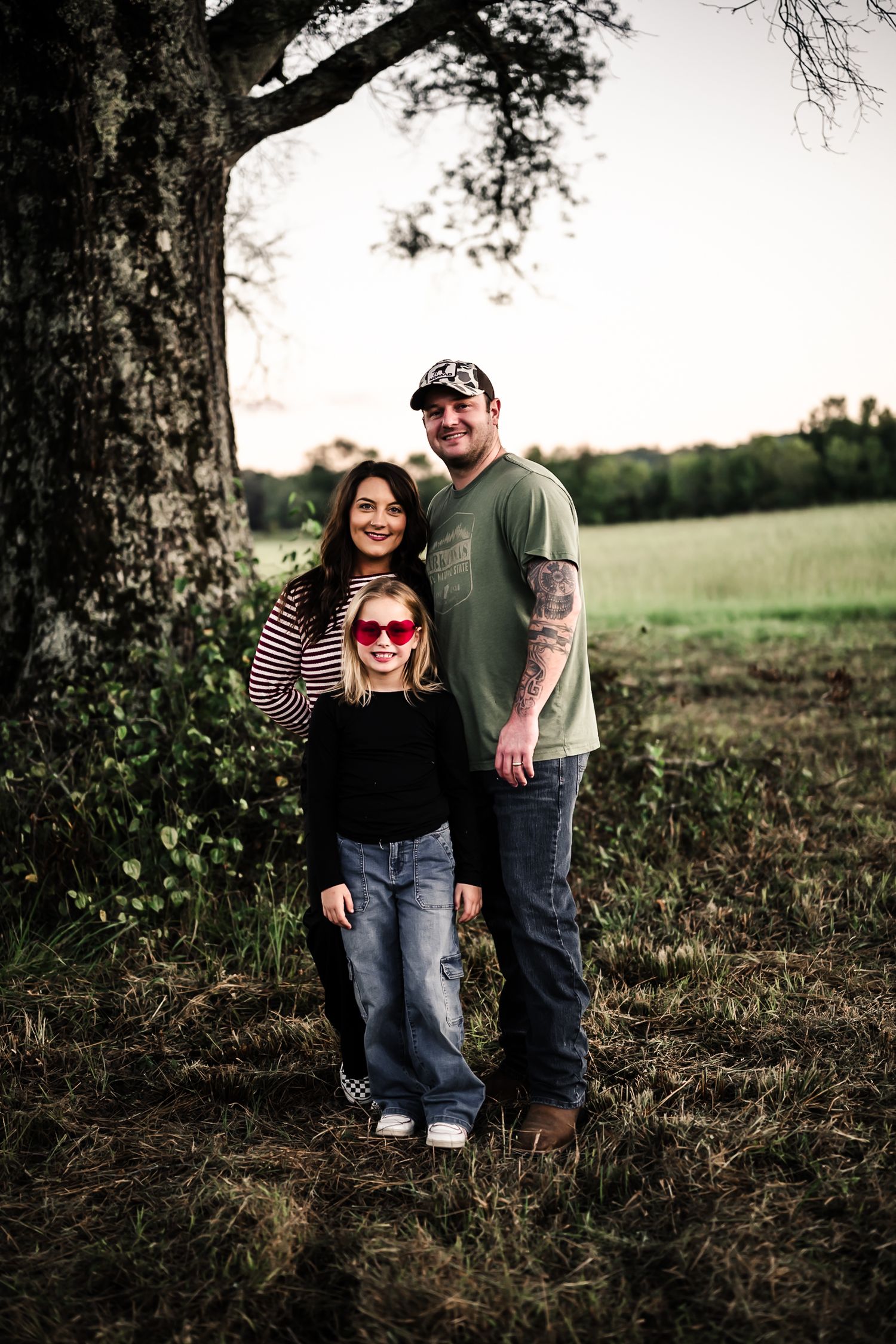 Couple posing under large tree in rustic outdoor setting during golden hour.