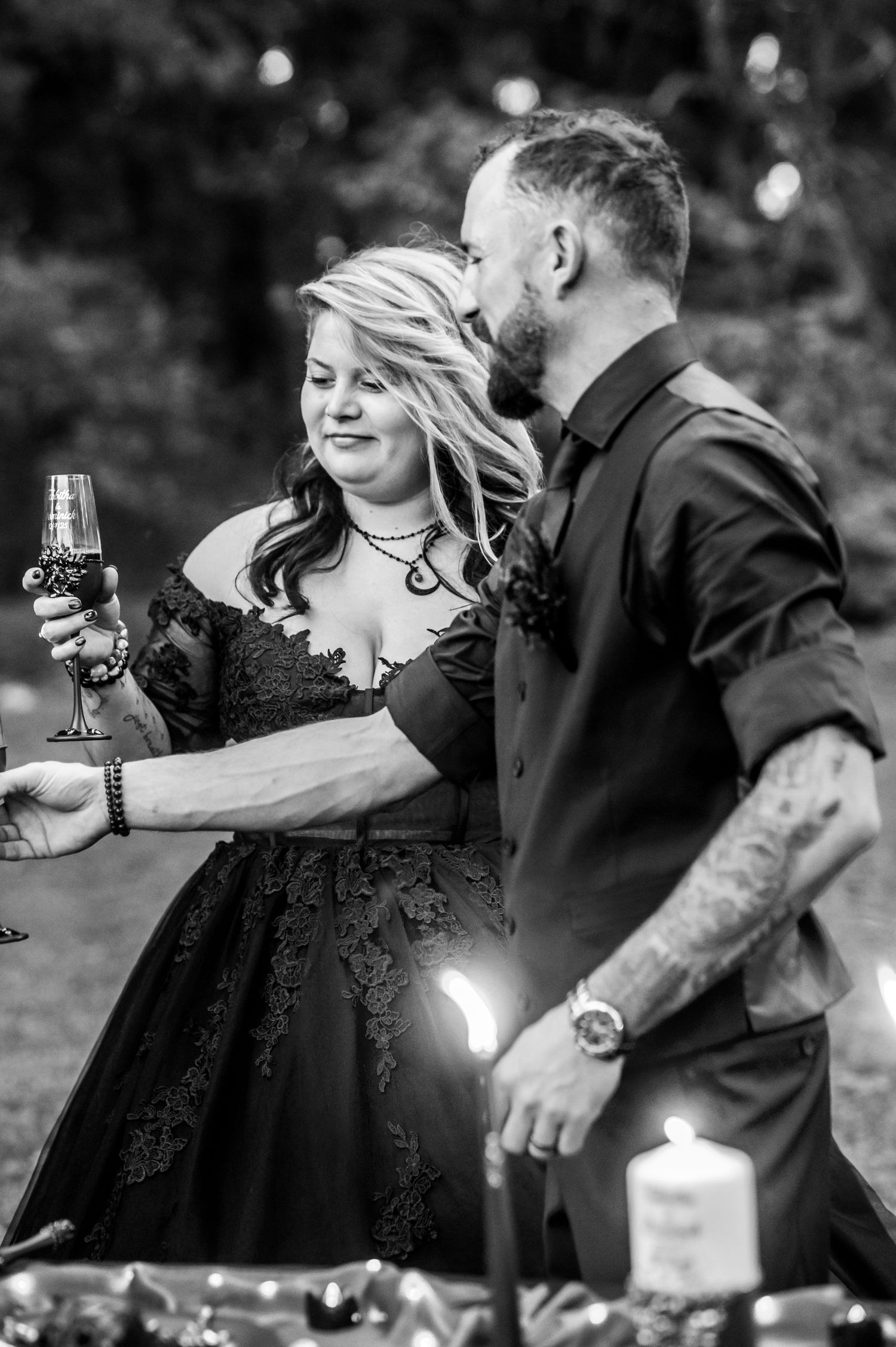 Romantic couple in black attire sharing wine and intimate moments during an outdoor photoshoot.