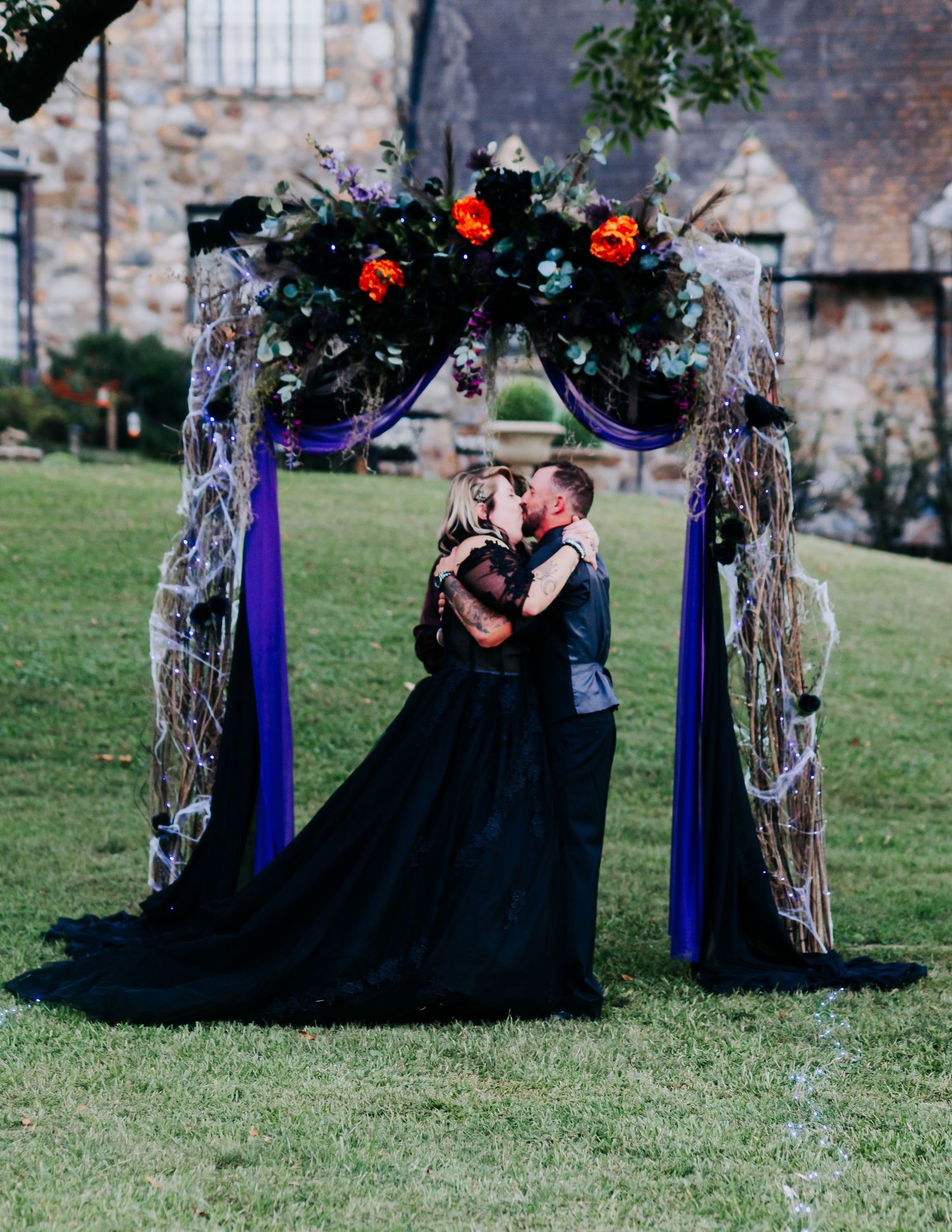 Gothic wedding photoshoot with couple in black attire among decorated trees.
