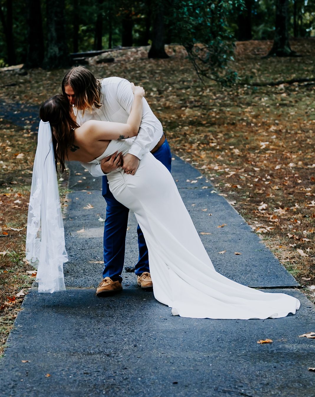 Wedding couple's romantic dip sequence on path surrounded by autumn leaves.