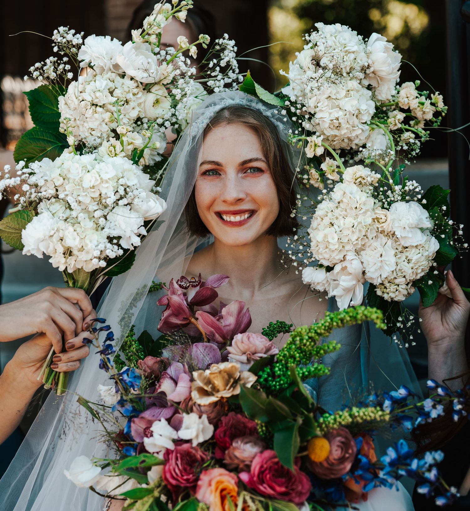 A bridal bouquet featuring white hydrangeas, burgundy lilies and blue accents creates an elegant contrast.