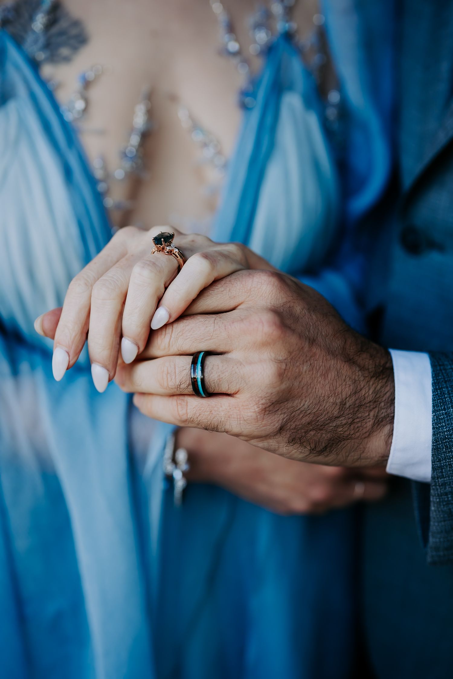 Close-up sequence of hands showing black wedding bands against a blue background during a romantic moment.