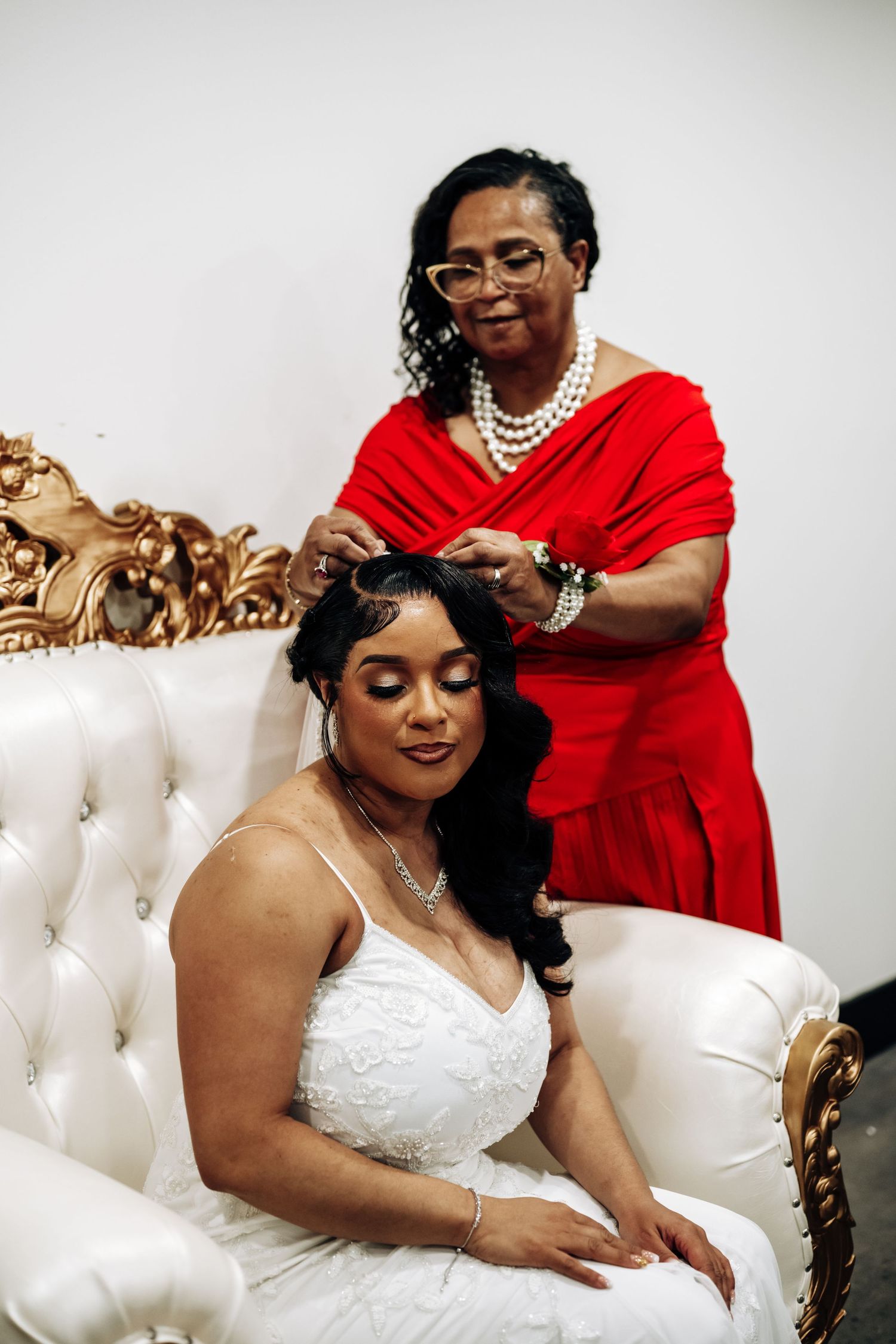 A bride in a white strapless wedding dress poses on an elegant tufted cream sofa while getting ready for her ceremony.