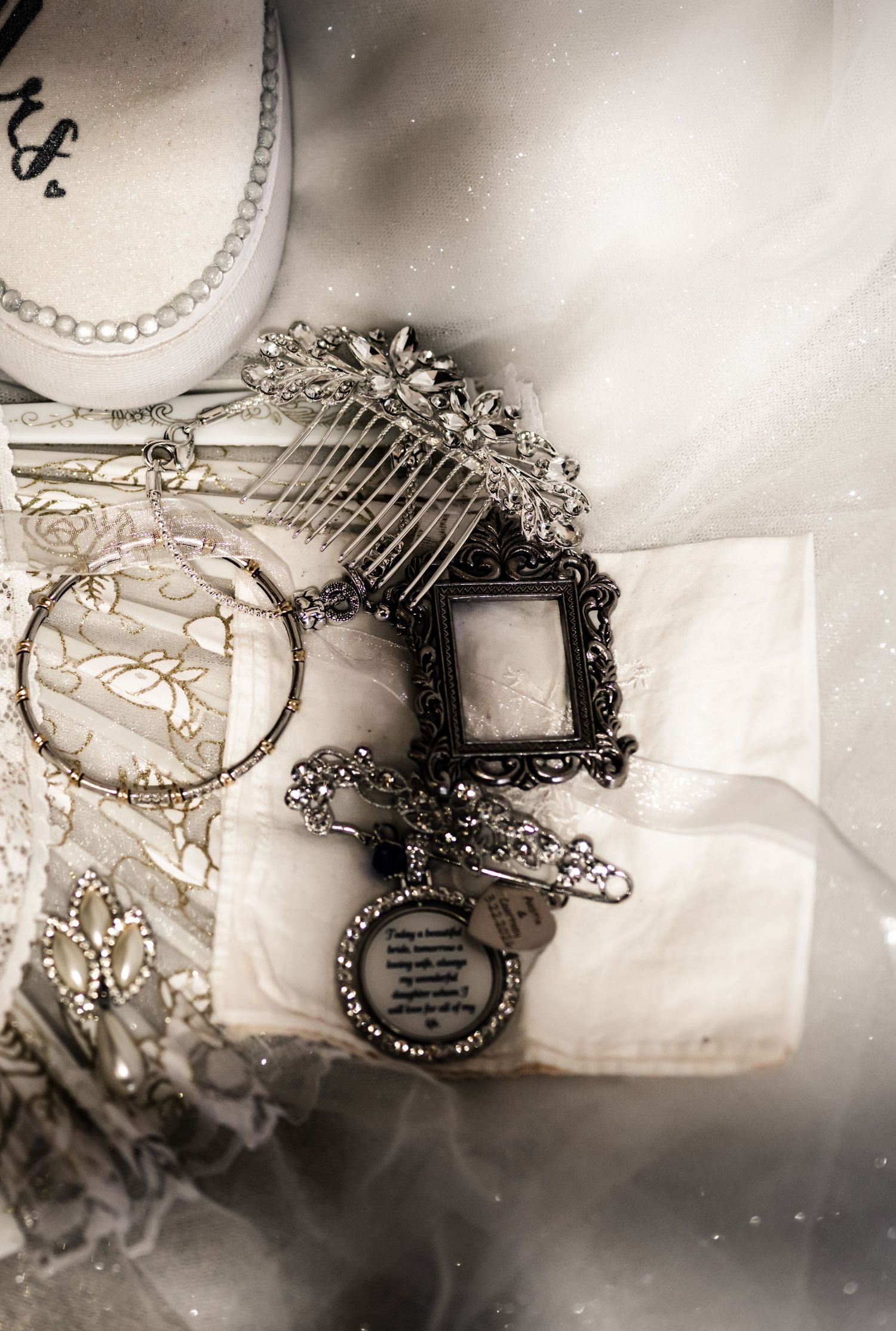 Elegant bridal accessories including a crystal hair comb, ornate picture frame charm, and lace details on white fabric.