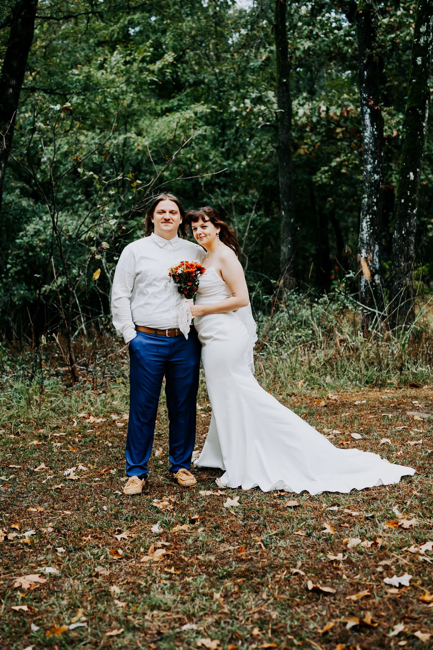 Wedding couple posing together on autumn ground covered with fallen leaves.