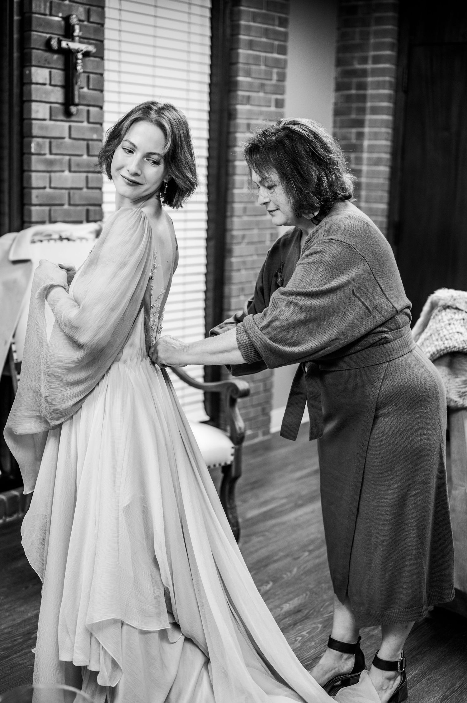 A black and white photo shows mom buttoning her daughter's wedding dress.