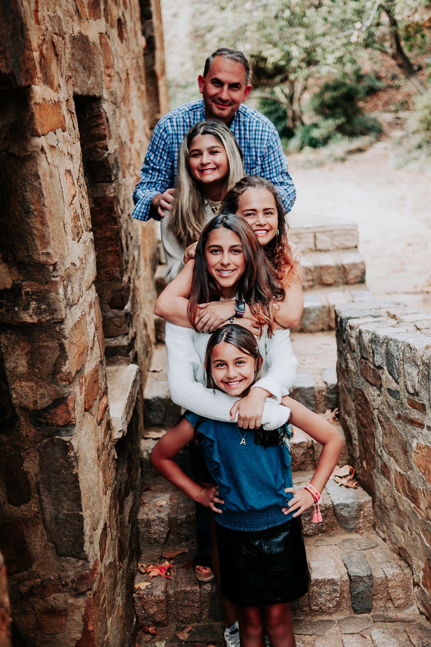 Family photoshoot with joyful expressions and playful poses on stone steps in an outdoor setting.