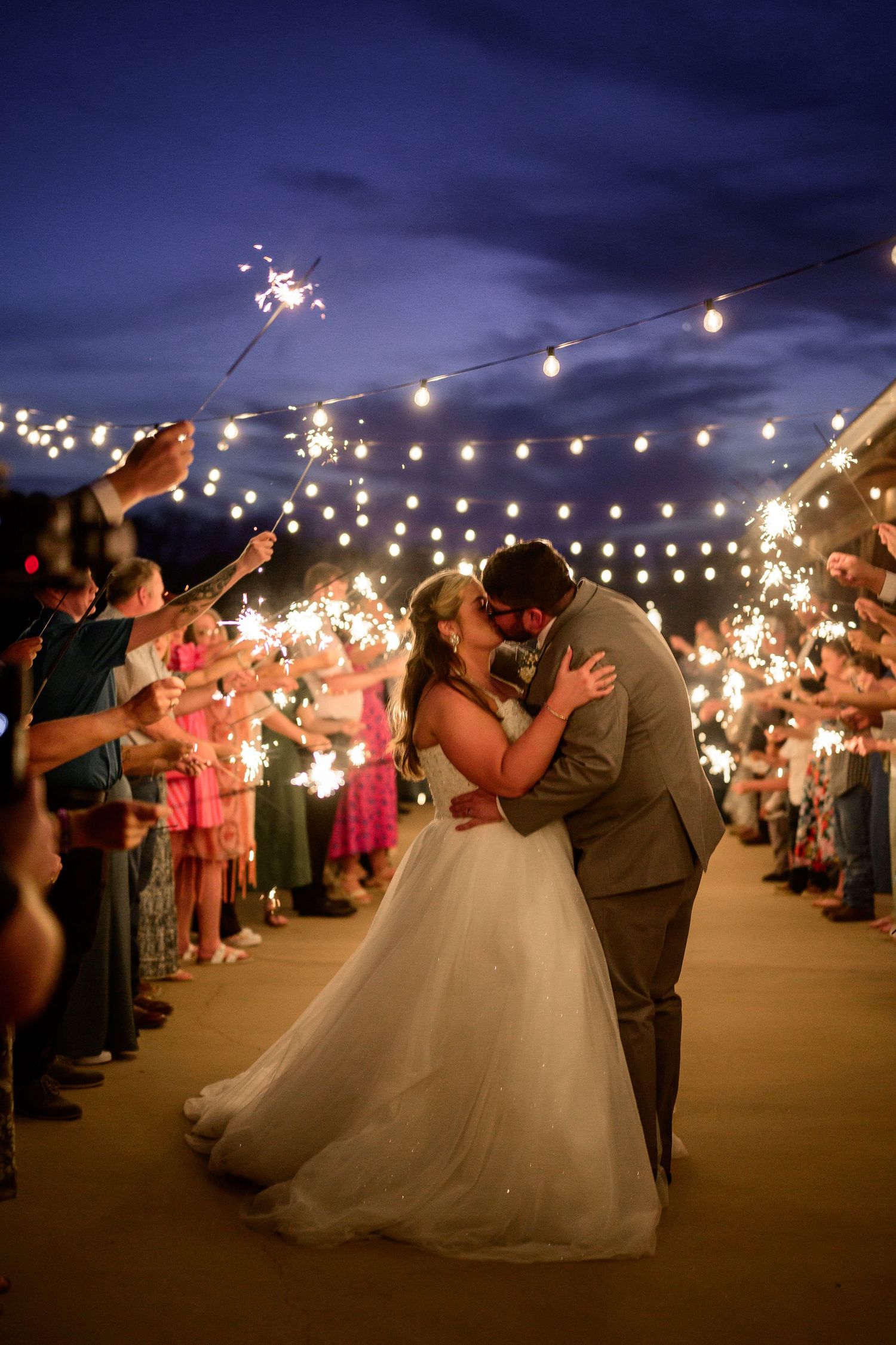 Bride and groom share a kiss during a romantic sparkler exit at their outdoor evening wedding reception.