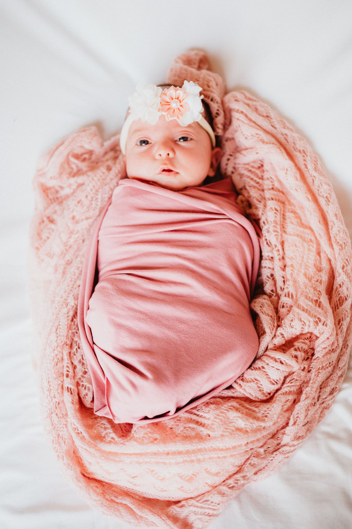 A newborn baby wrapped in soft pink fabric against white bedding.