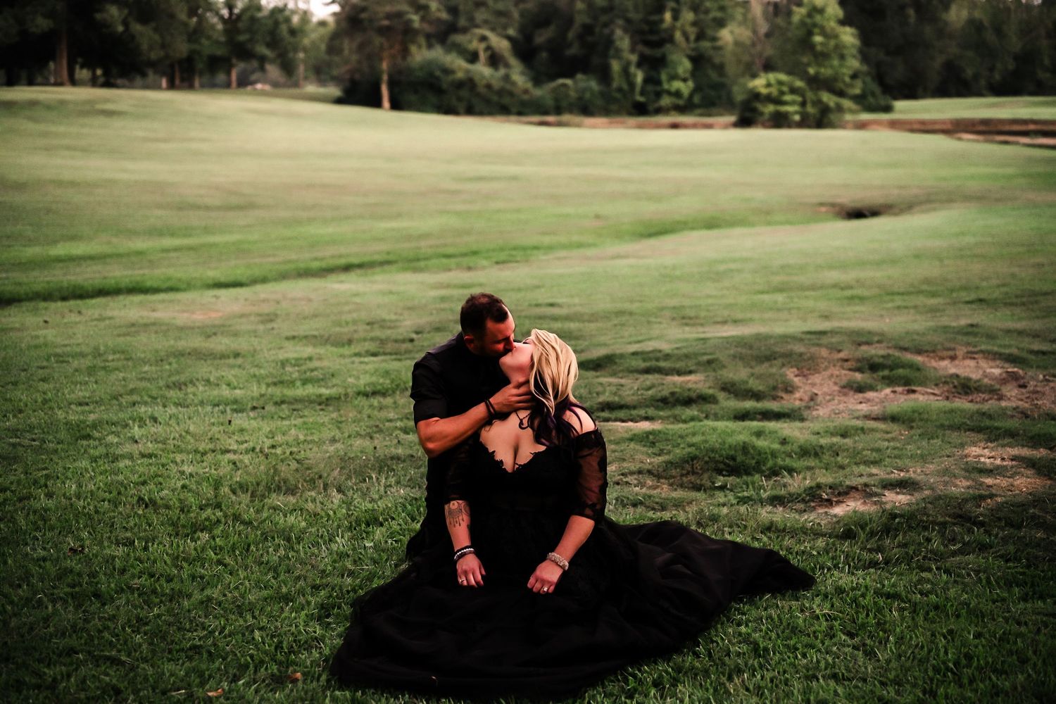 Couple embracing on a grassy hillside during sunset in a romantic outdoor setting.
