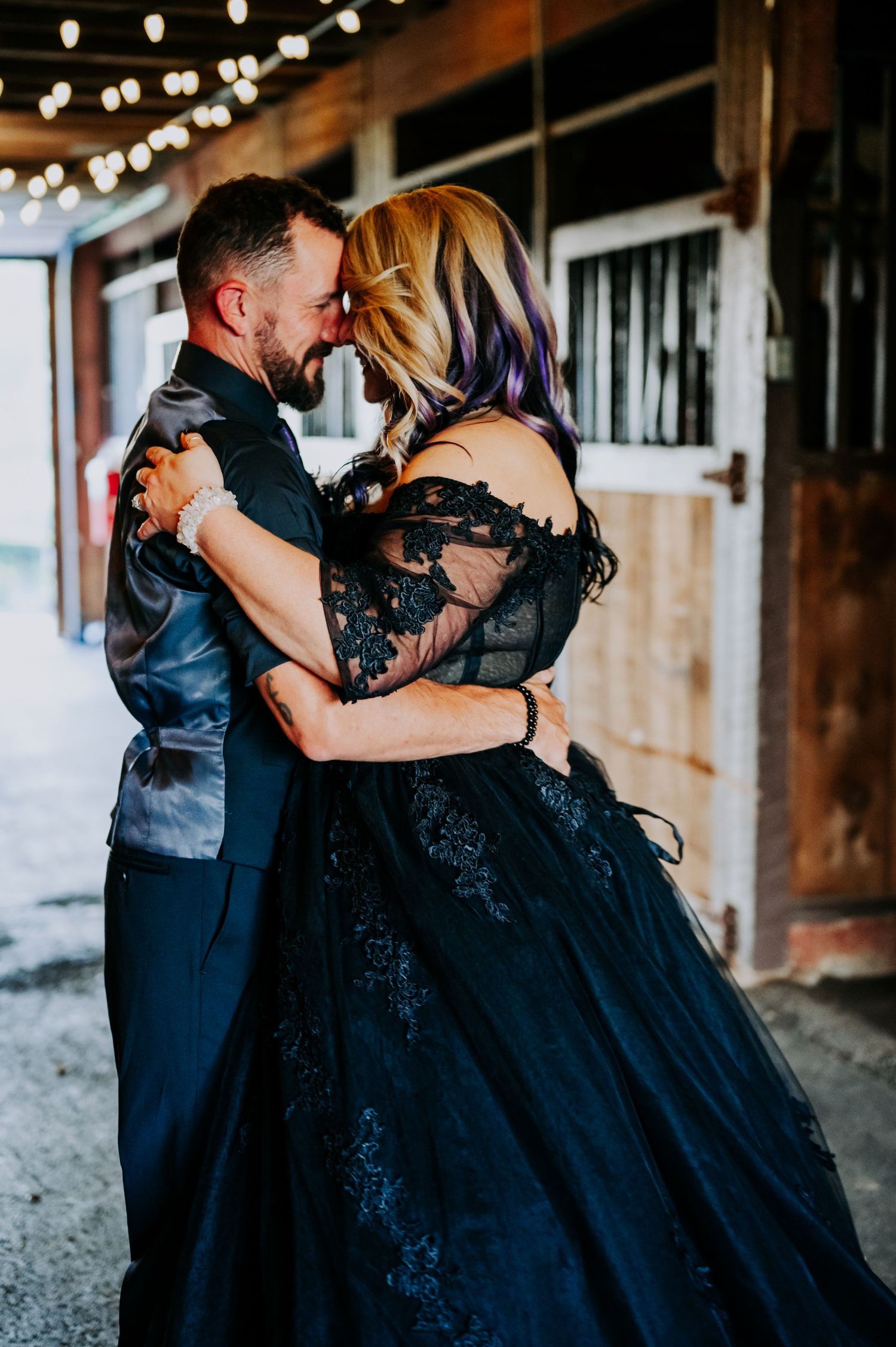 A romantic couple dances together in a rustic barn venue decorated with string lights.